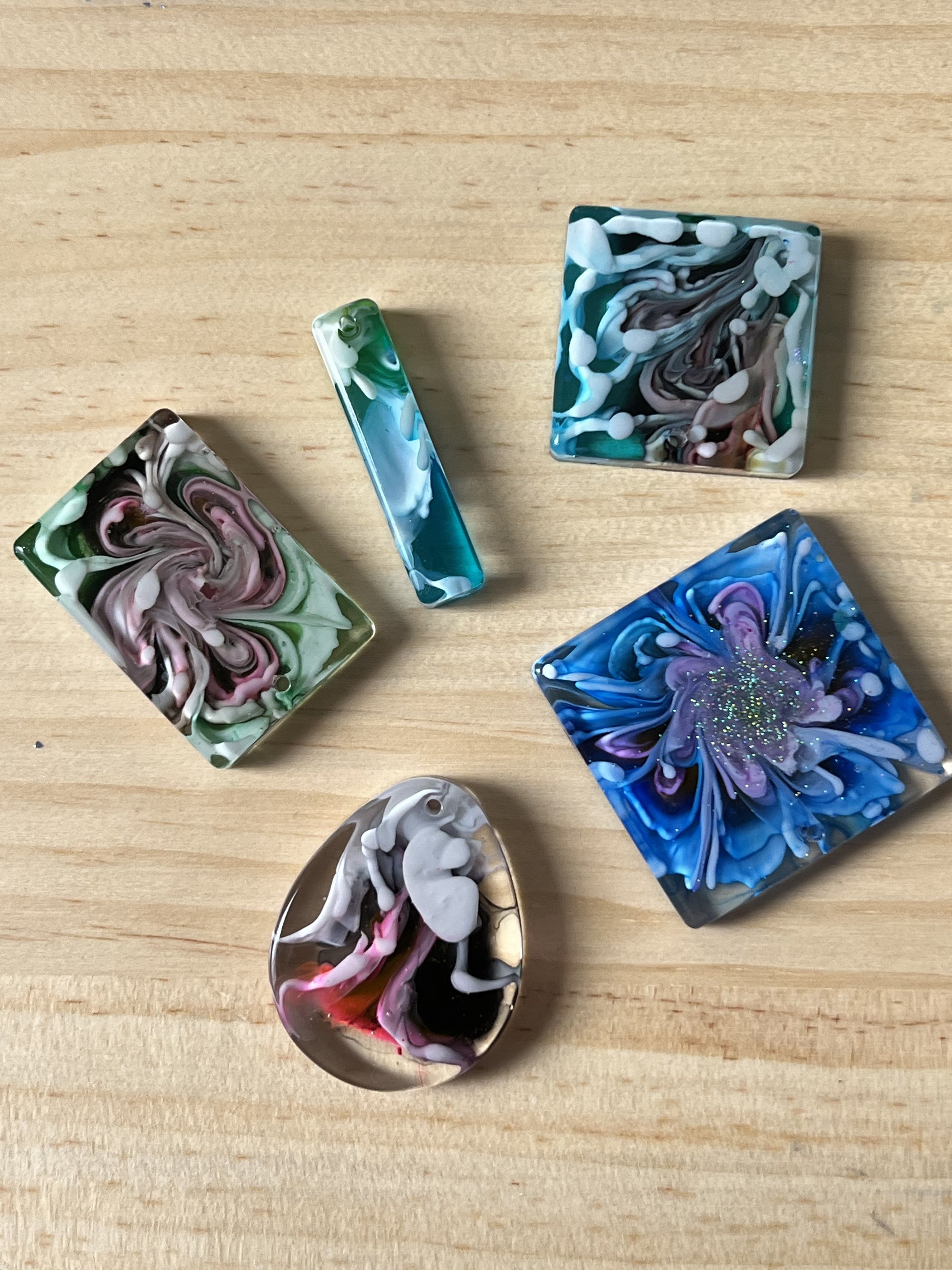 Six colorful marbled glass pieces with swirling patterns and various colors, arranged on a wooden surface.