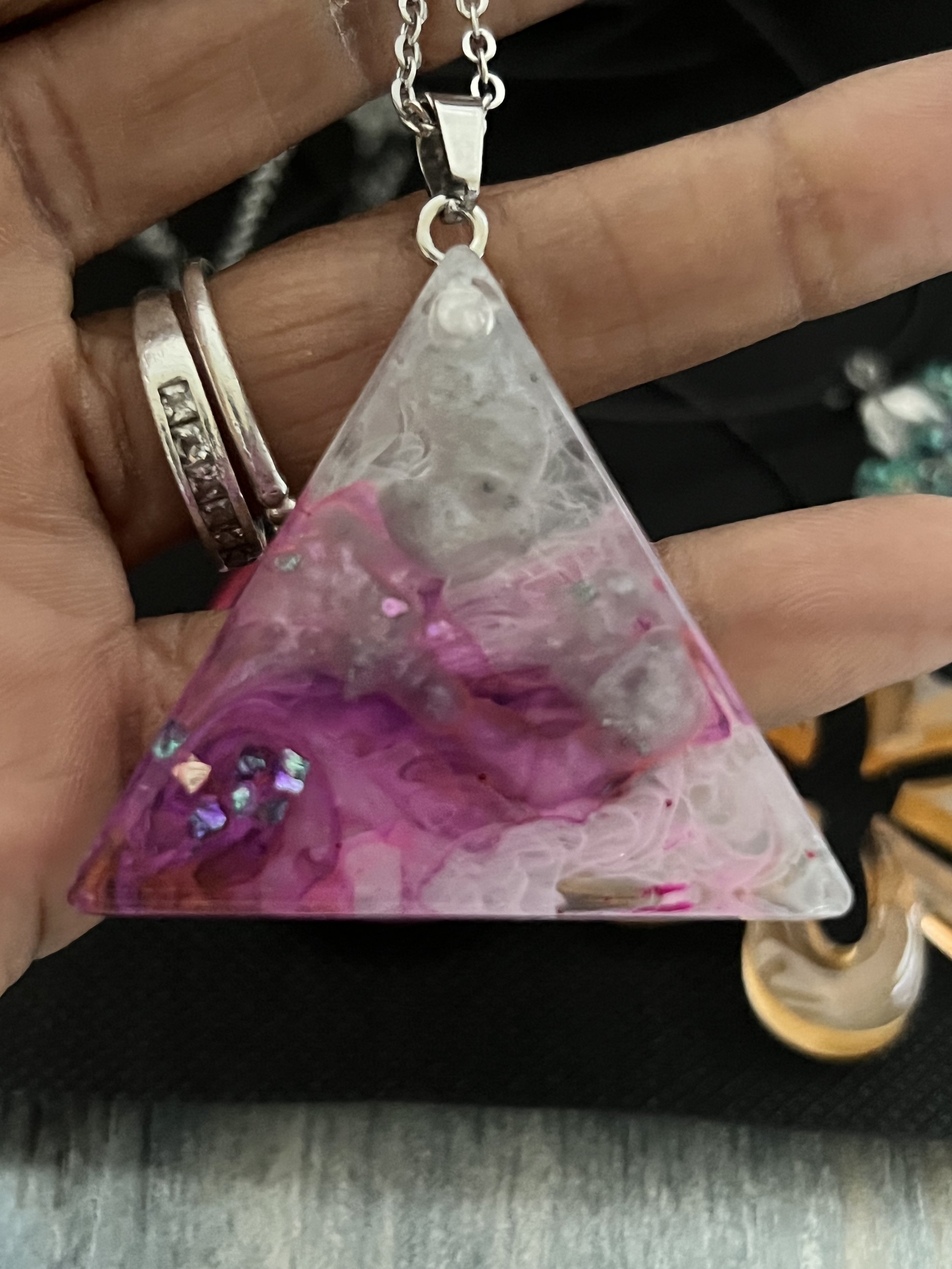 Close-up of a person's hand holding a triangular resin pendant with pink, purple, white, and iridescent colors embedded inside.