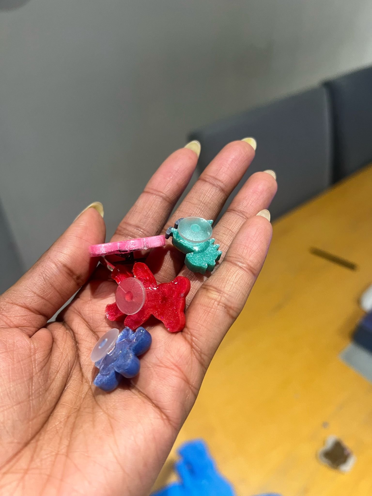 A hand holding colorful plastic cookie cutters in various shapes, including a fish, a bear, and a bird.