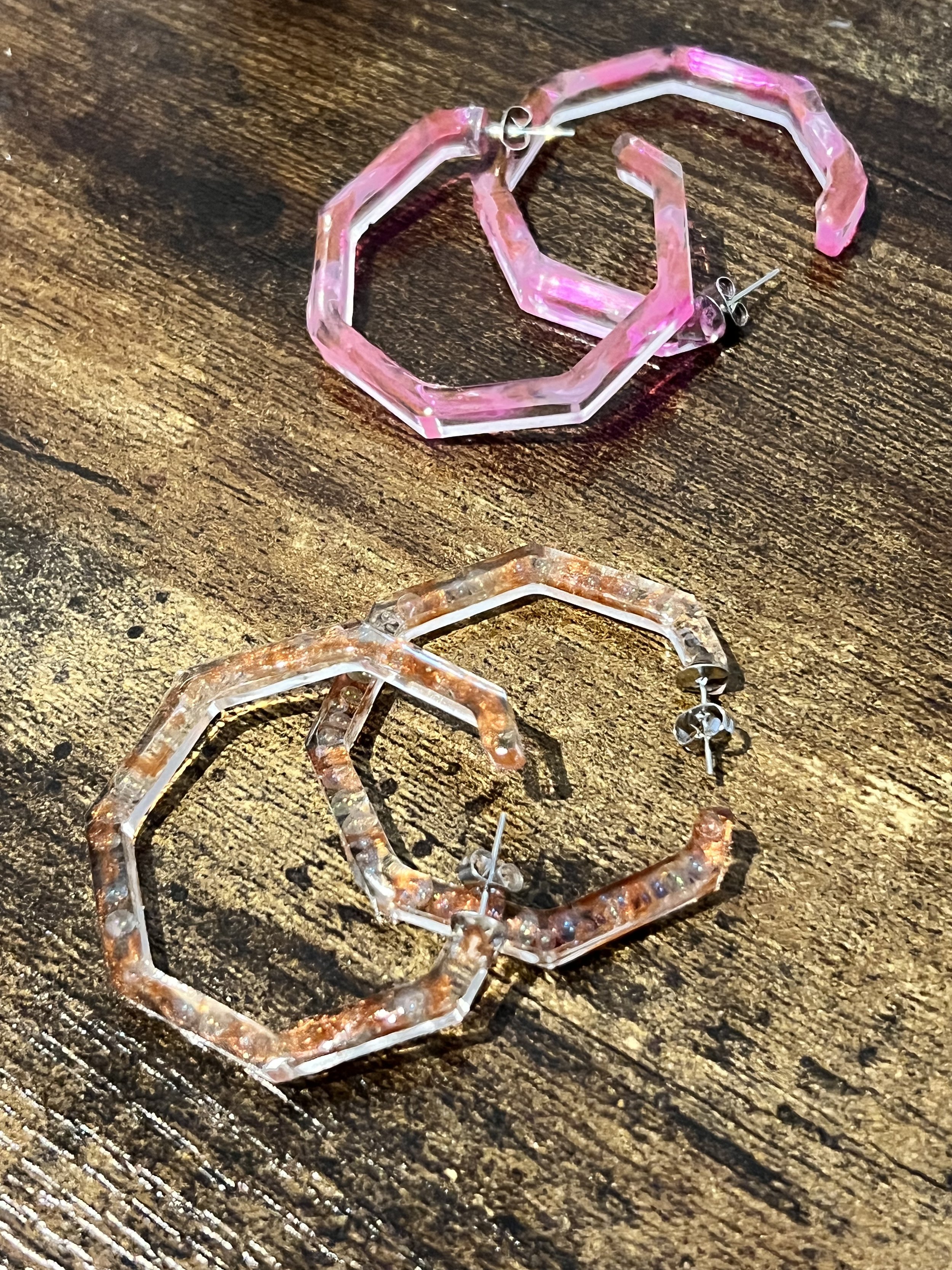 Pink and brown transparent geometric earrings on a wooden surface.