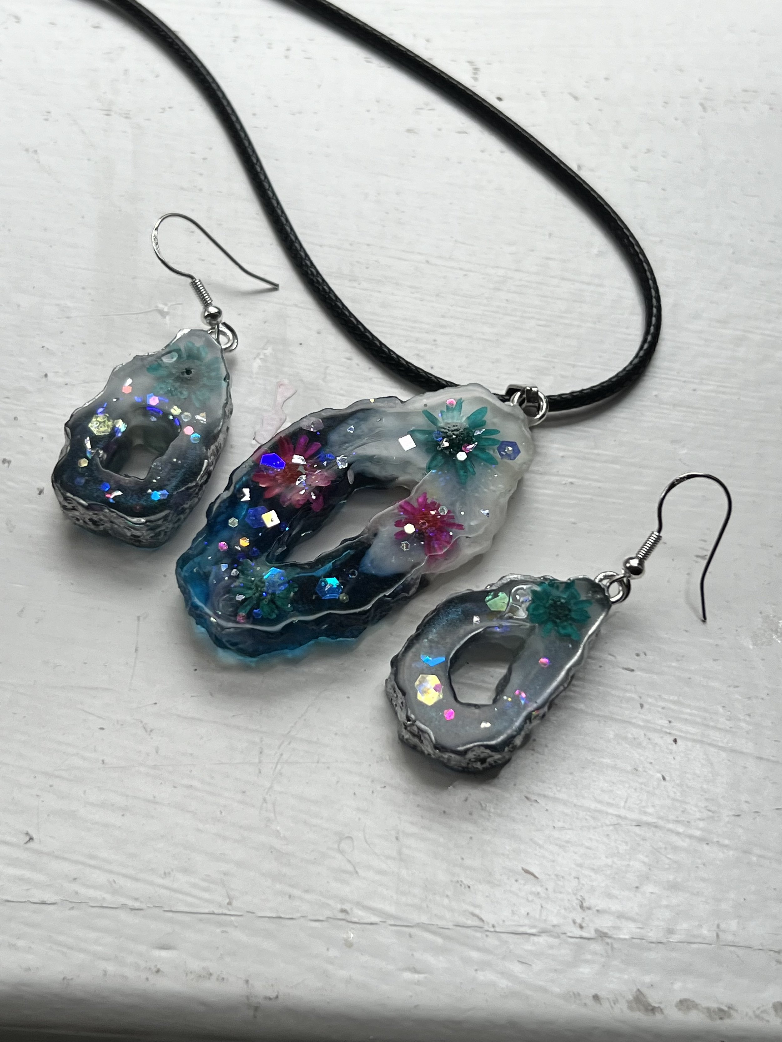 A set of jewelry including a necklace and a pair of earrings with resin and embedded colorful glitter and flower designs.