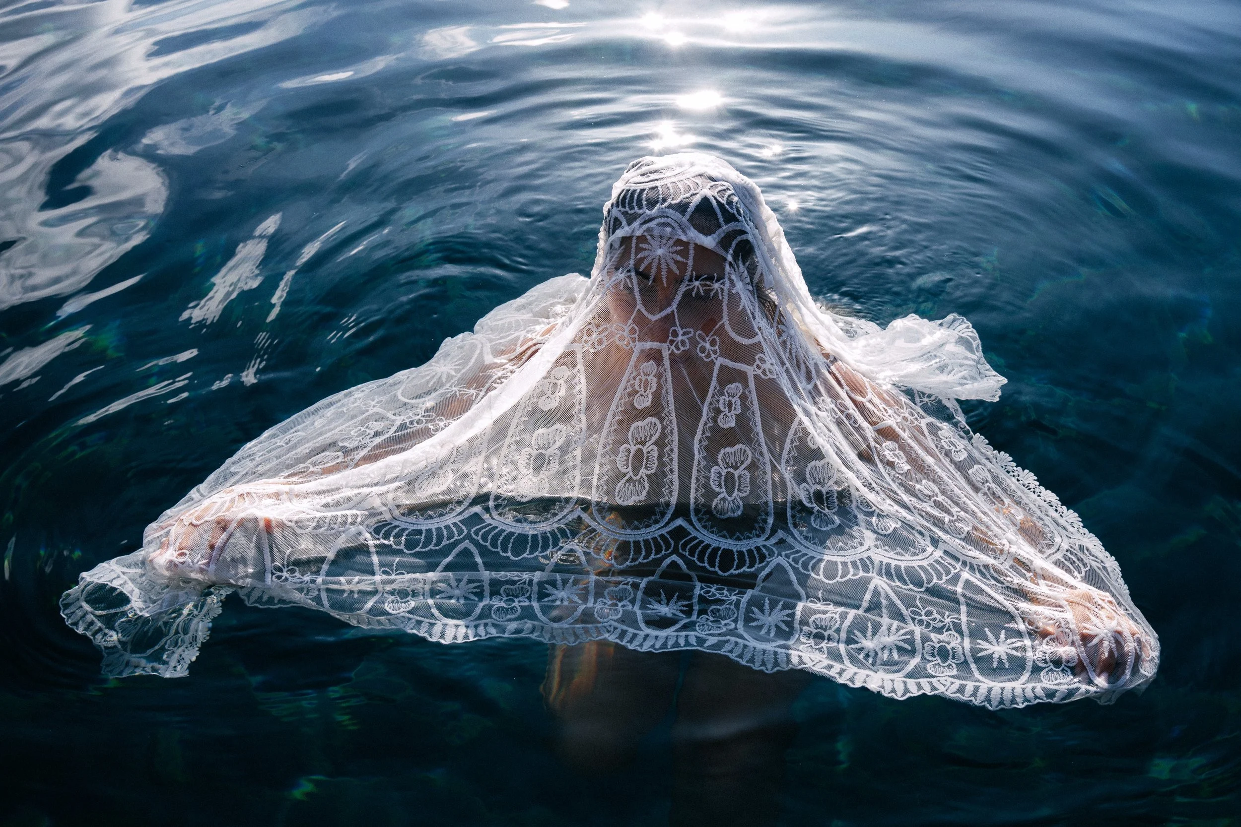Person with a lace veil covering their face, submerged in Mediteranean sea.