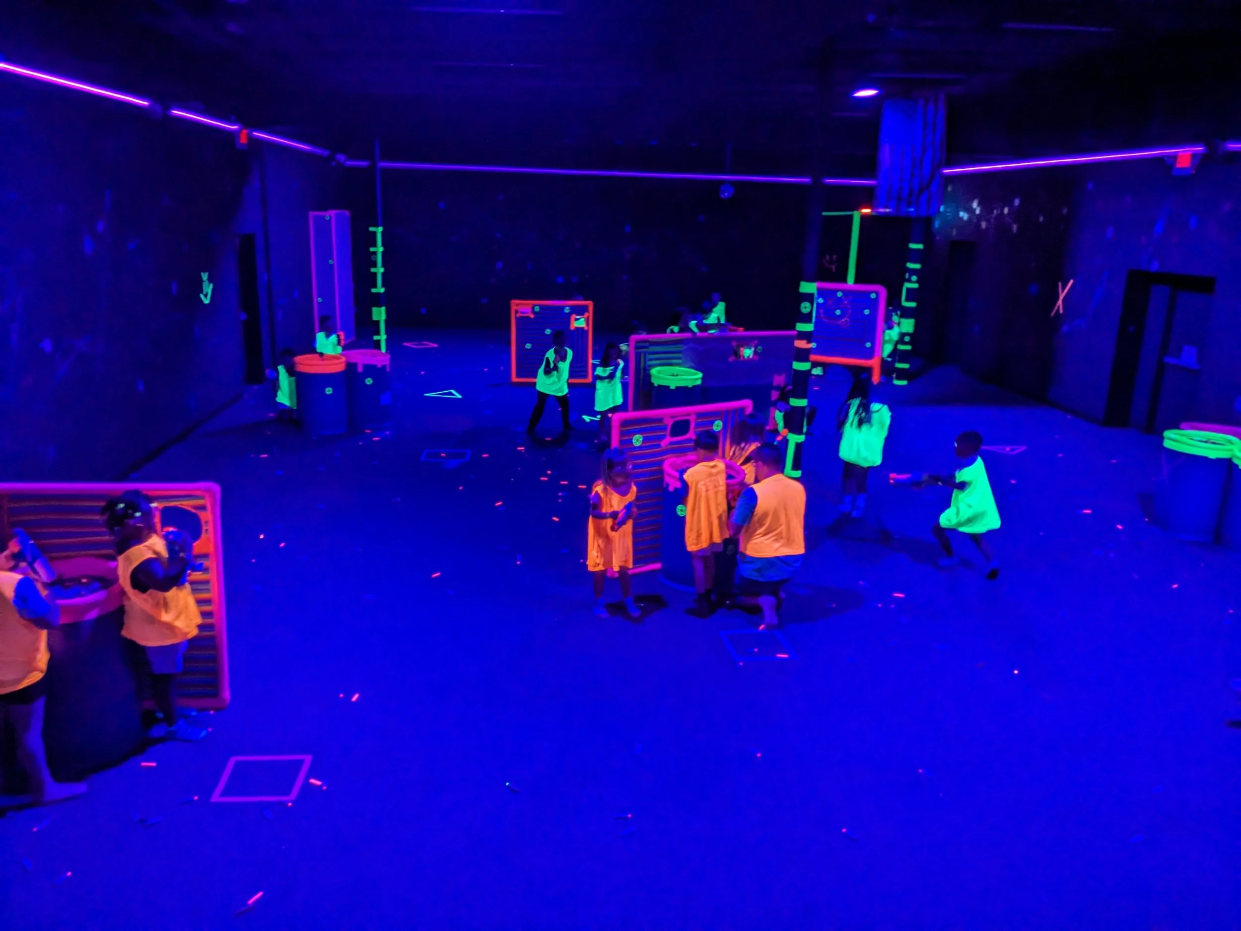 Children playing laser tag in a blacklight arena with neon decorations and glow-in-the-dark equipment.