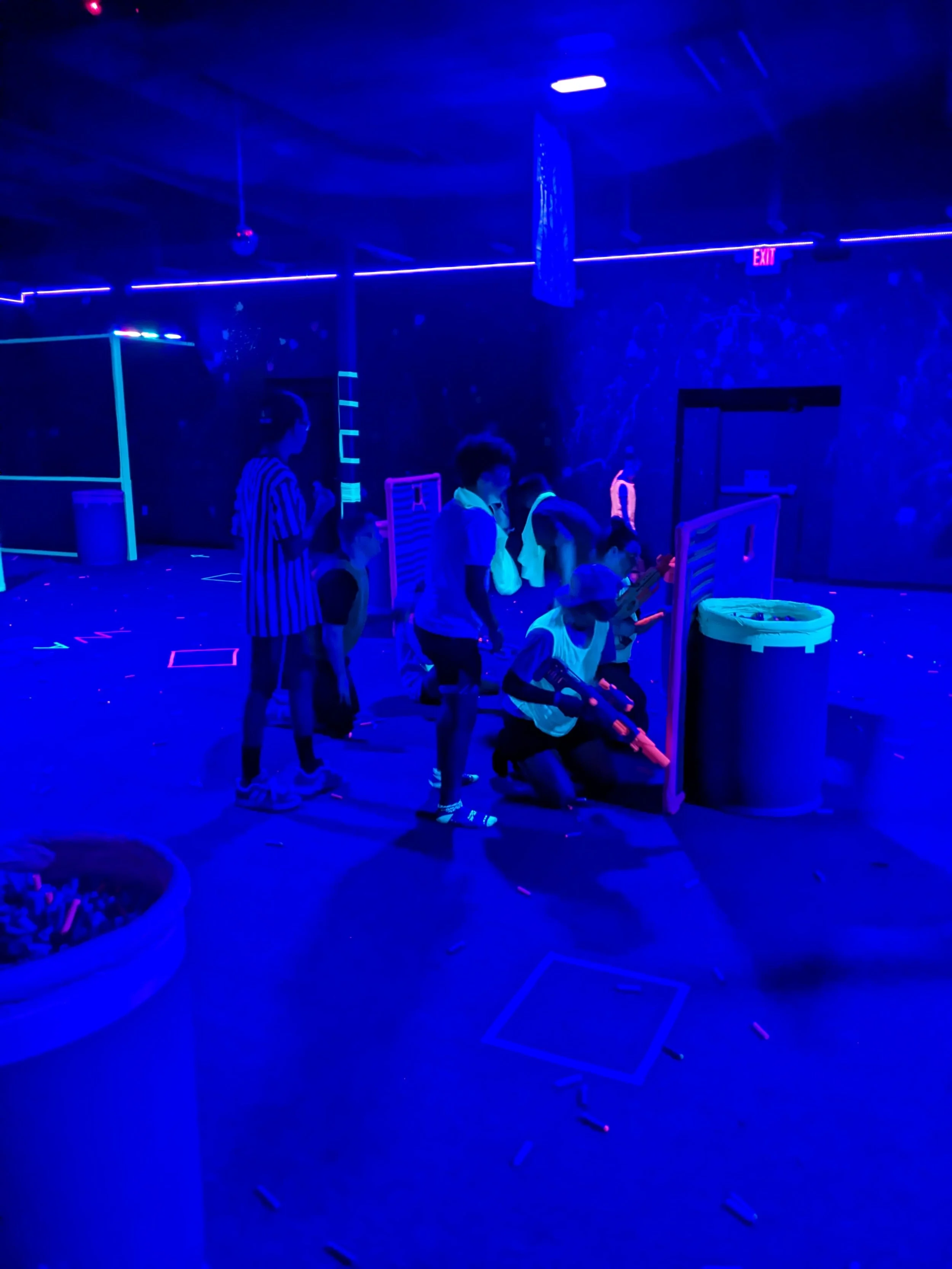 Children playing laser tag in a dark, neon-lit arcade with blacklight and glow-in-the-dark decorations.