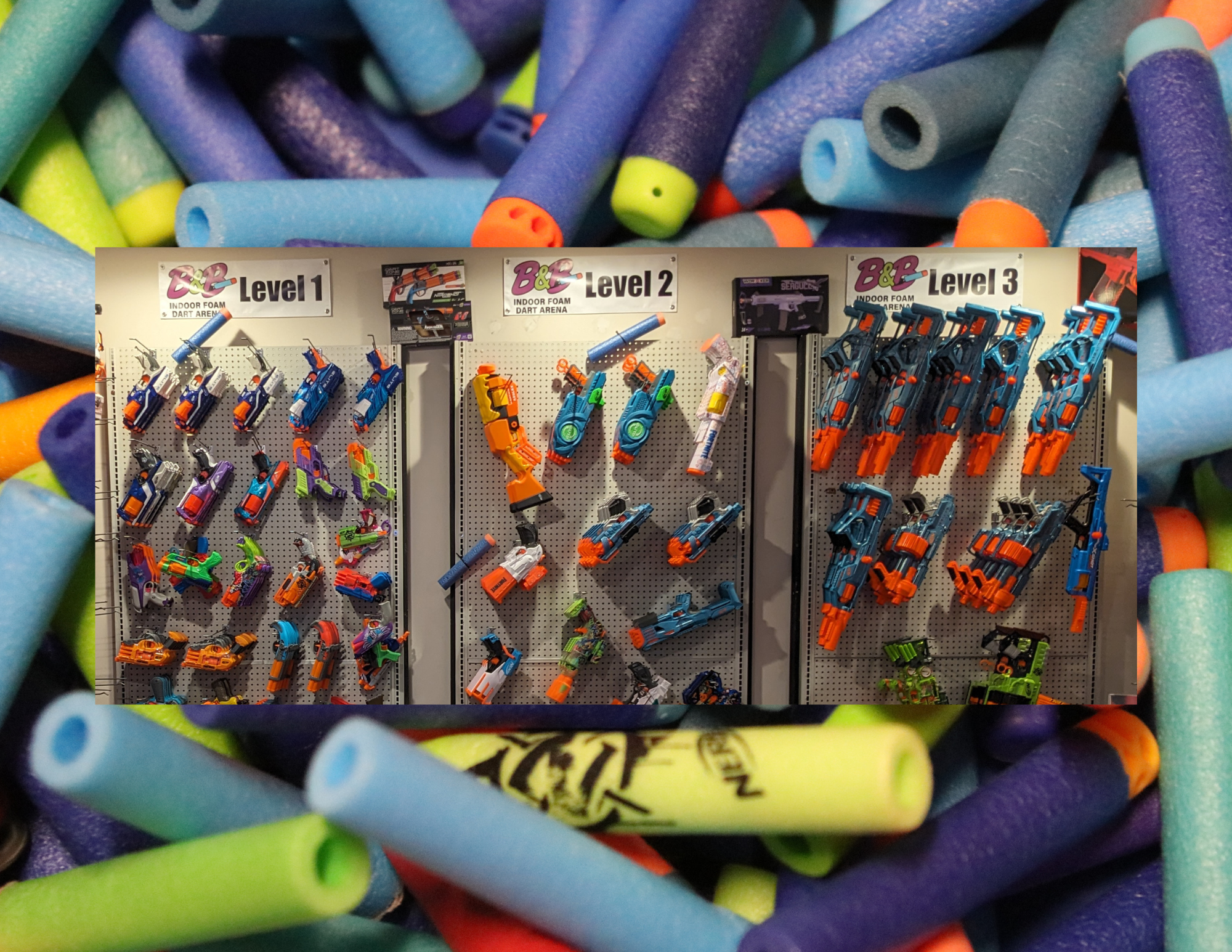 Close-up of colorful foam and Nerf blasters on shelves in a toy store, with signs for levels 1, 2, and 3 of indoor foam dart arena.