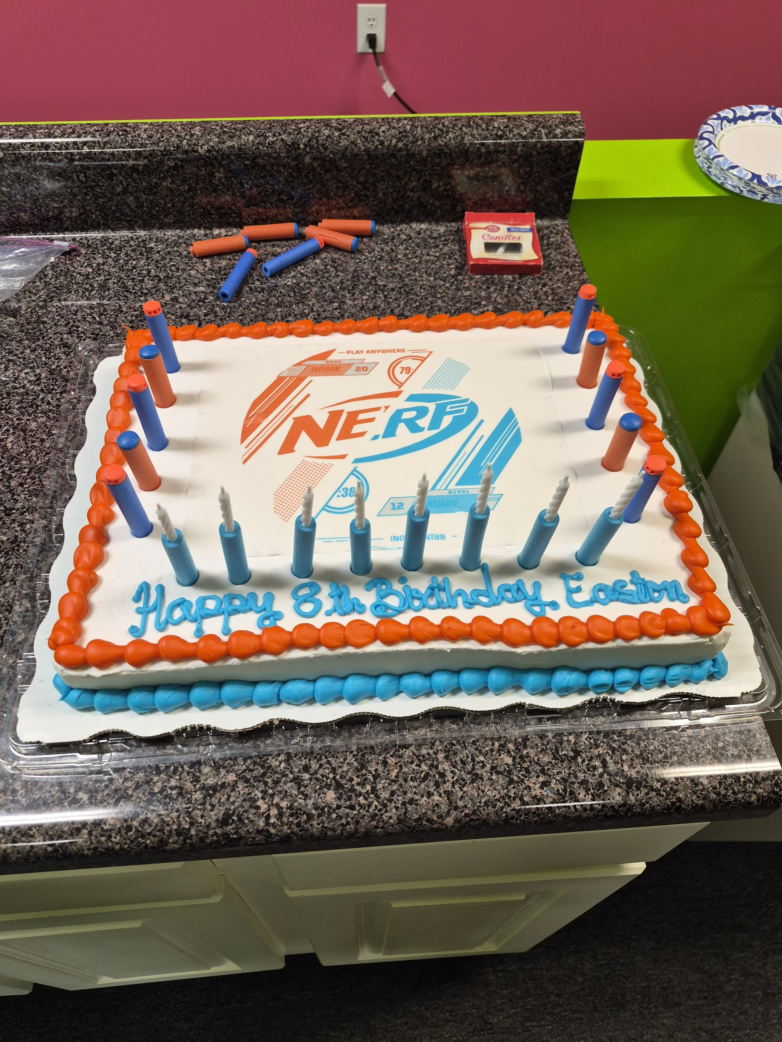 A birthday cake with Nerf logo, orange and blue borders, and candles, celebrating Easton's 8th birthday.