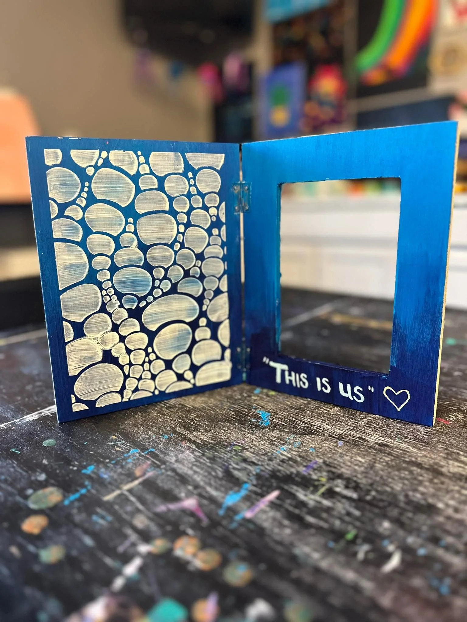 A small blue decorative picture frame with a cutout on the right side and a pattern of overlapping circles on the left side, placed on a multicolored, speckled work surface.