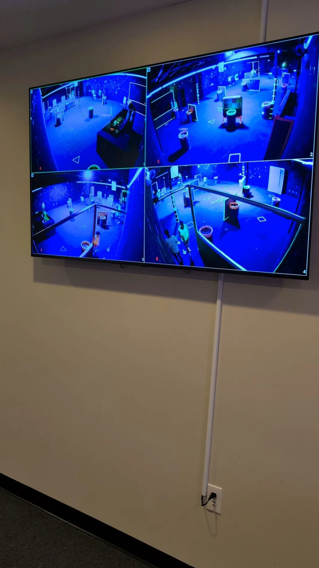 Security monitors showing a gaming or entertainment room with blue neon lighting, multiple gaming stations, and musical instruments.