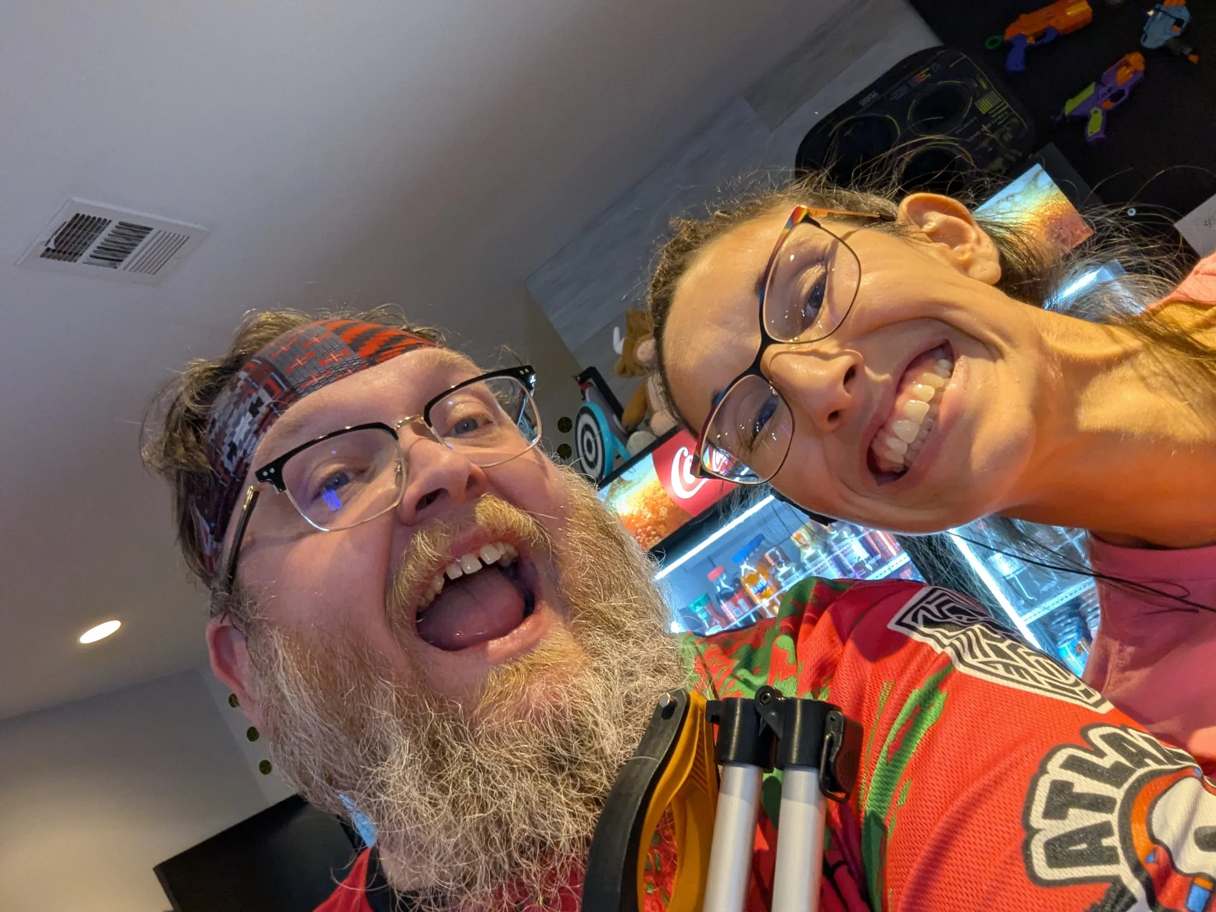 Two smiling people taking a selfie in a game arcade, with colorful arcade machines and games in the background.