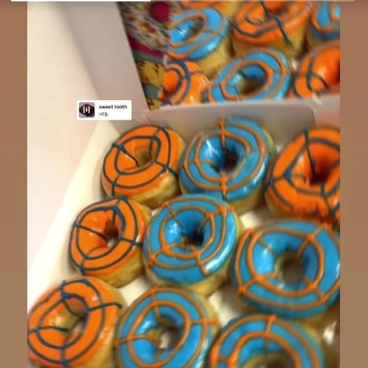Box of colorful donuts with orange and blue icing and drizzles.