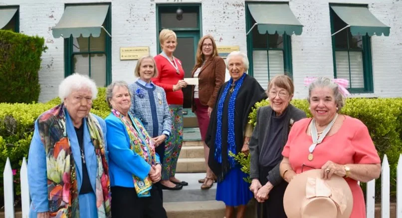 Group of seven women, mostly elderly, standing on steps in front of a white building with green awnings, smiling.