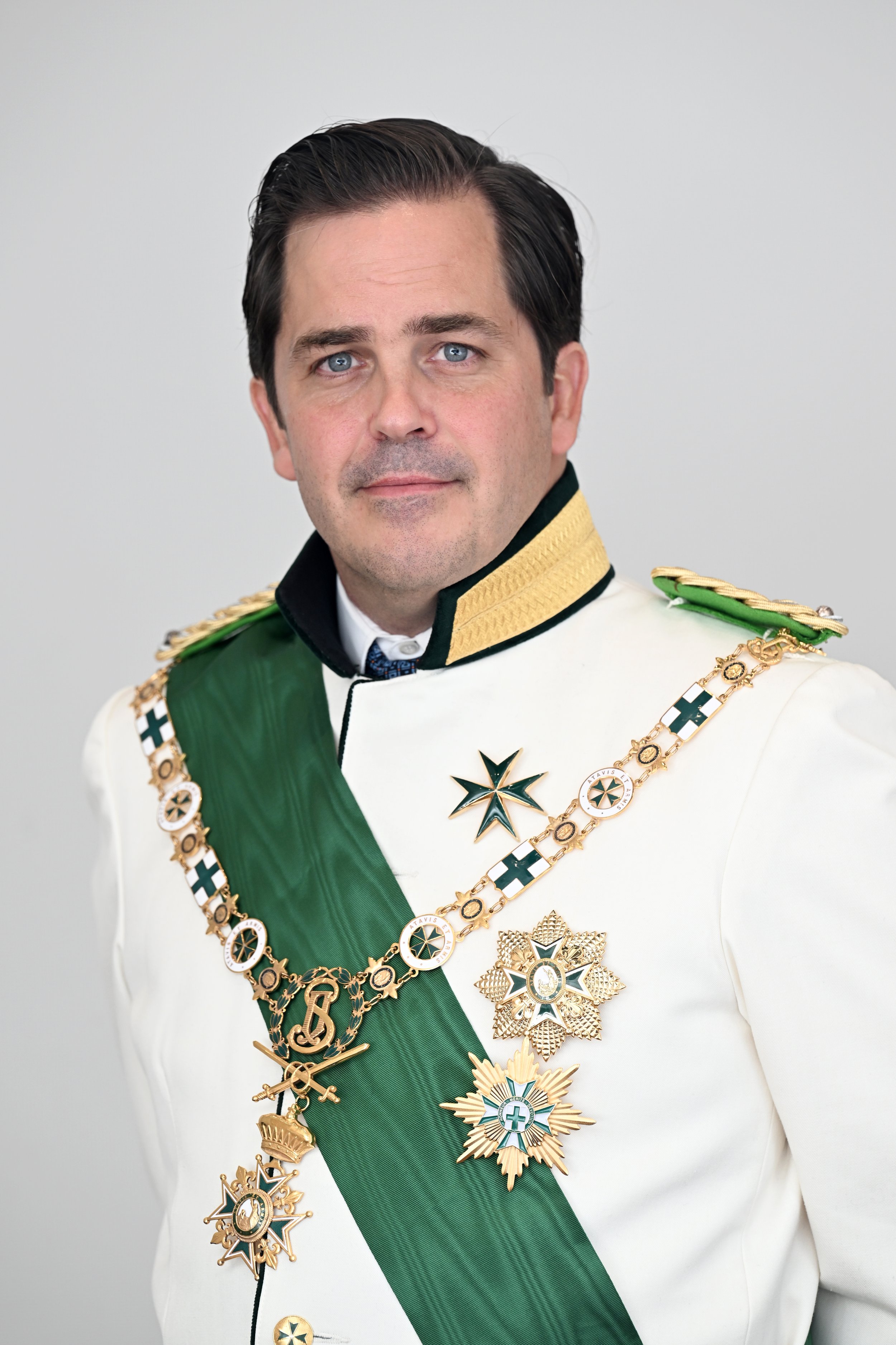 A man dressed in a formal military uniform with numerous medals and an emerald green sash.