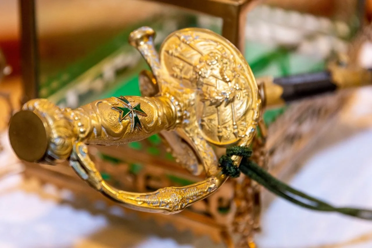 Close-up of a gold-colored ceremonial sword with detailed engravings and a star emblem, mounted on a decorative stand.