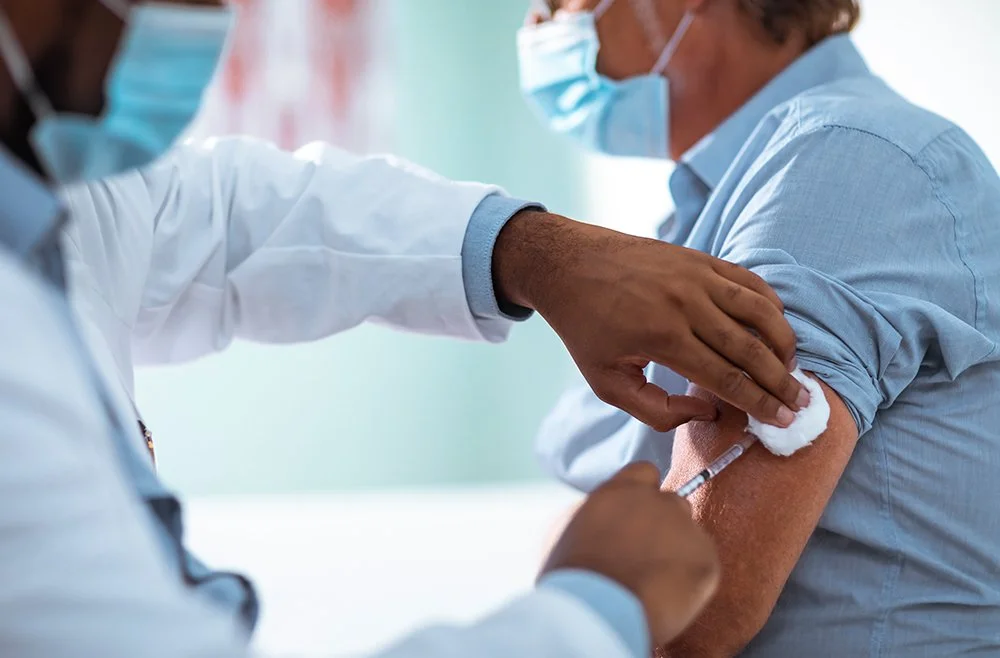 A medical professional giving a patient a vaccination in the arm while wearing a face mask.
