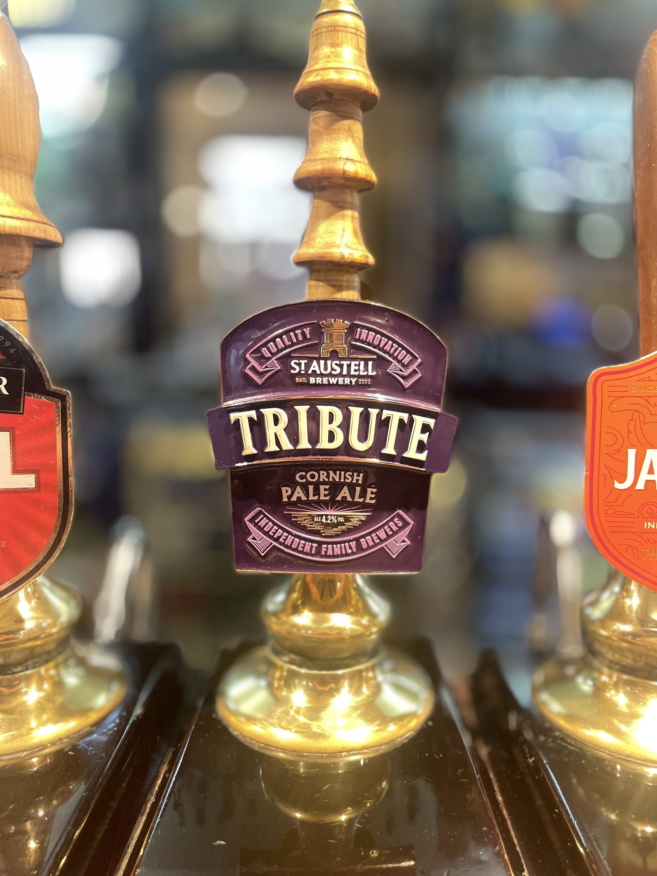 A bottle display with an orange and black label reading 'Saltaire Amarillo', a citrussy golden pale beer with 4.5% alcohol by volume, on a dark reflective surface inside a bar or store.