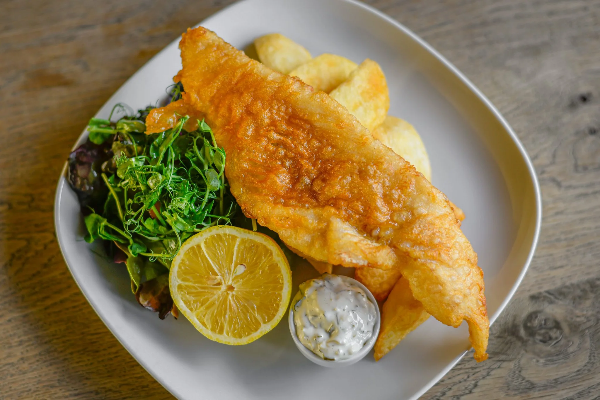 Fried fish fillet with potato chips, lemon slice, mixed greens, and tartar sauce on a white plate