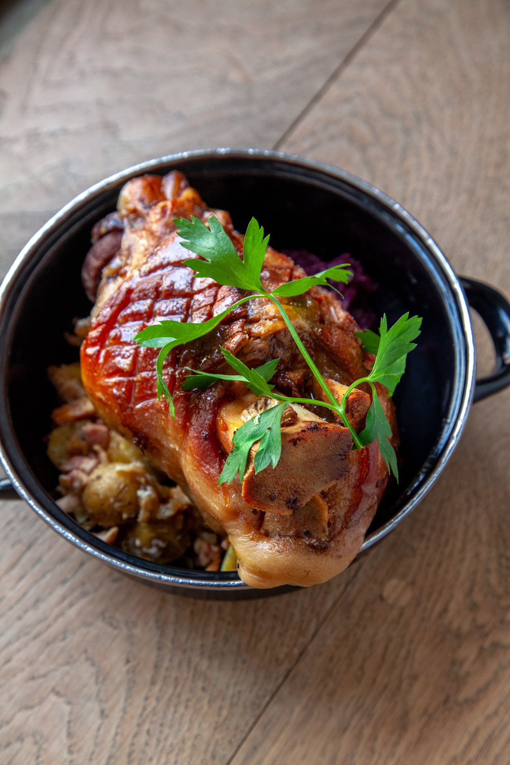 Baked meatloaf garnished with fresh parsley, served in a black enamel mug on a wooden surface.