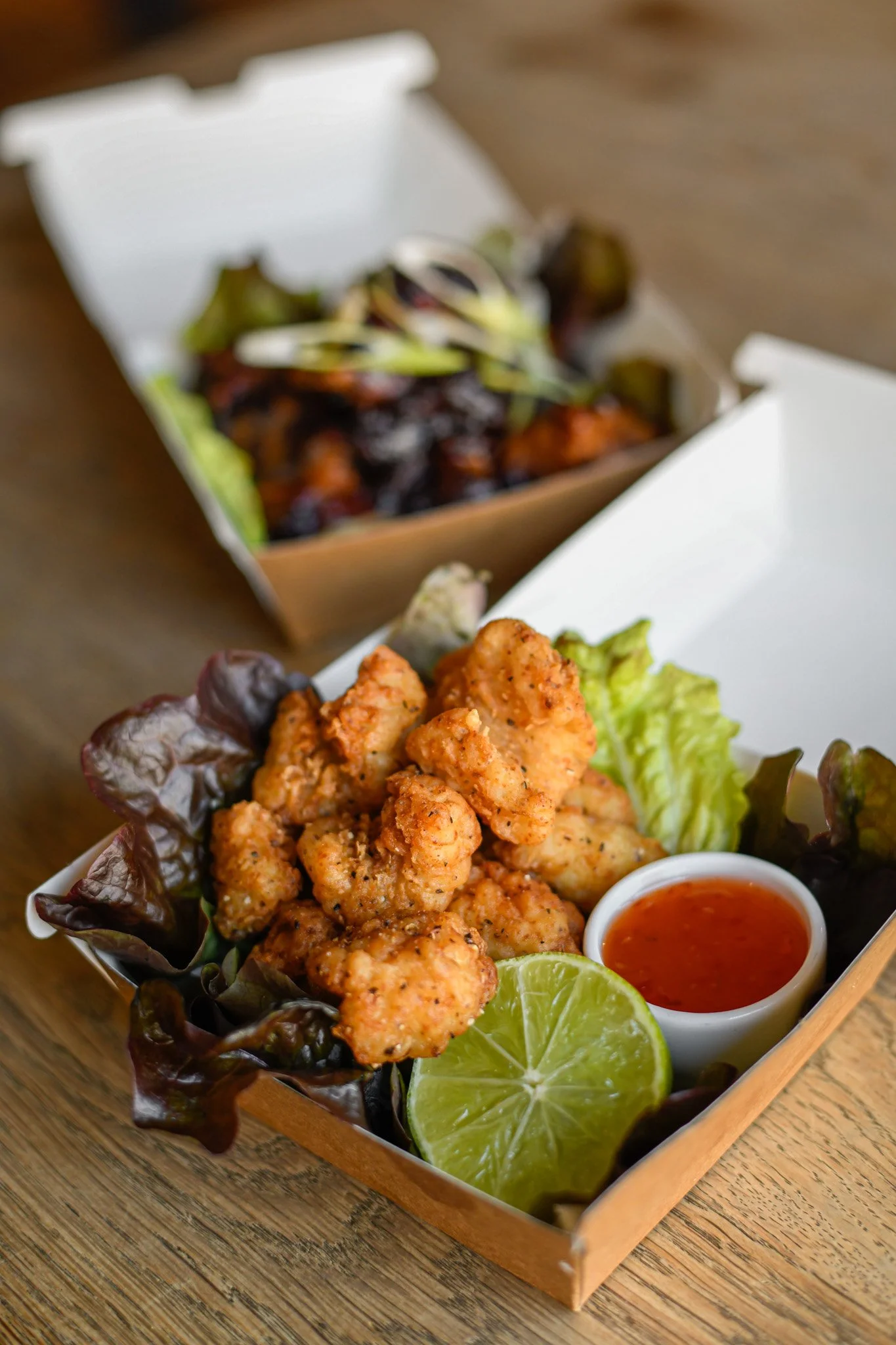 Fried chicken bites with lime wedge, lettuce, and dipping sauce in a takeout box.