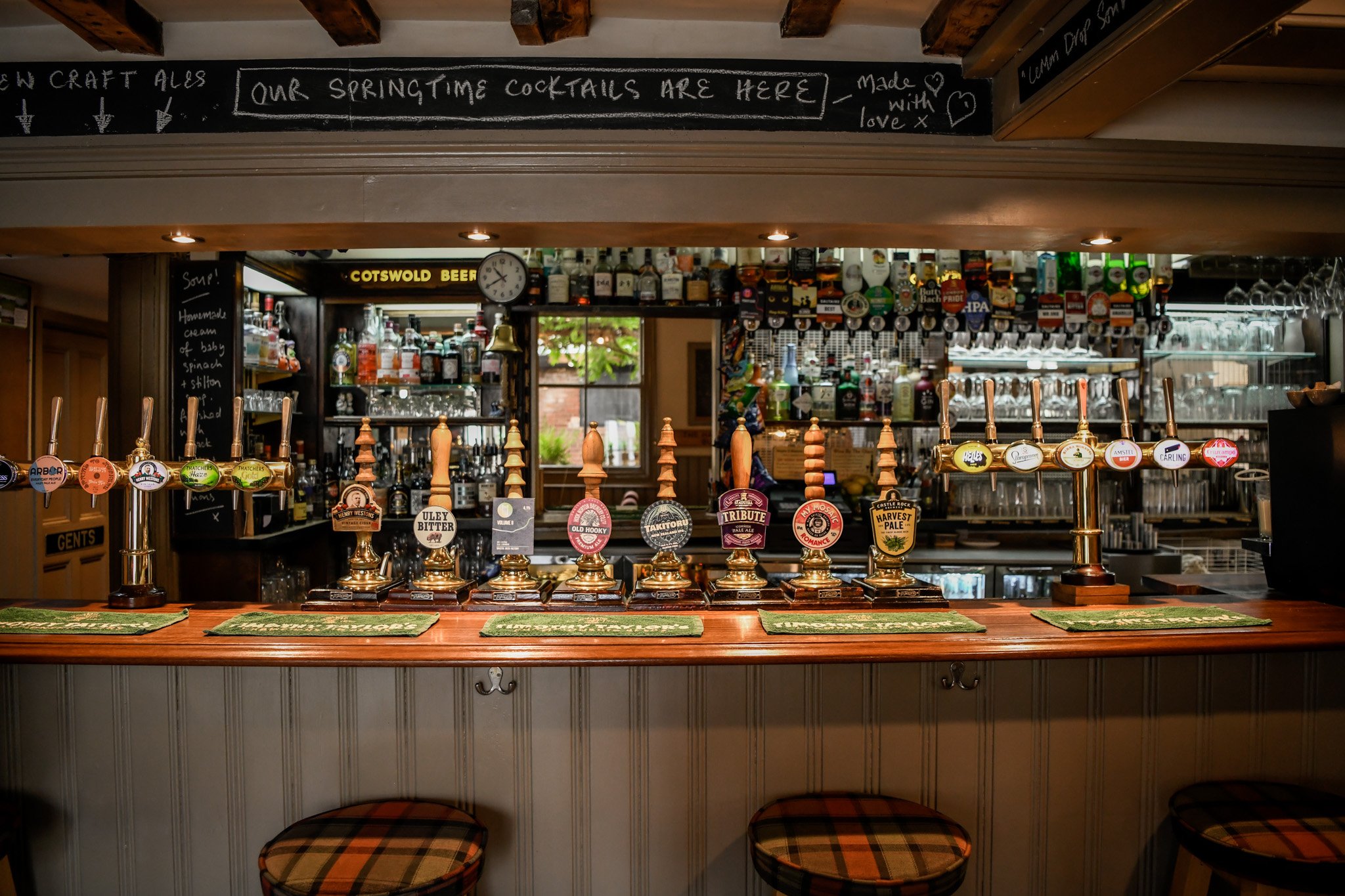 Bar with multiple beer taps, bottles above, glassware shelves, and a window in the background.