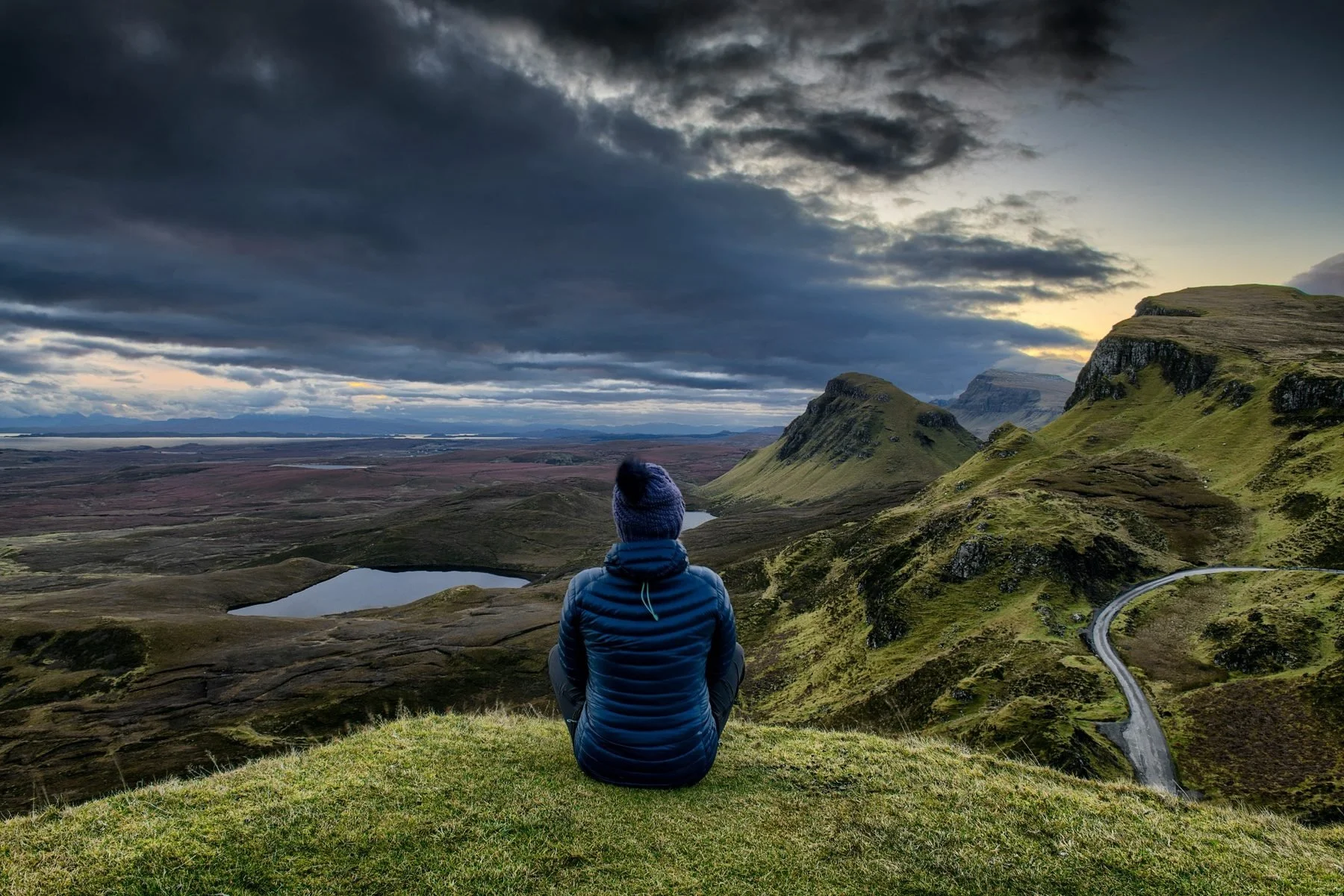Person sitting above a wide mountain landscape, representing reflection, perspective, and spiritual self-discovery.