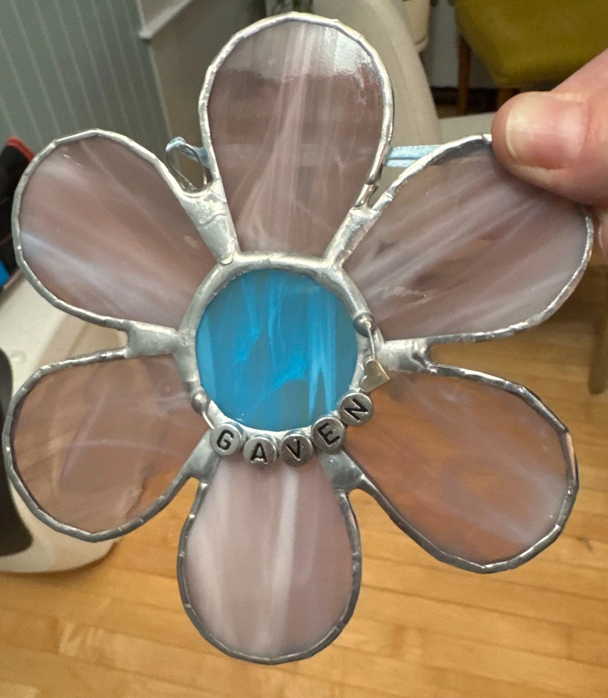 A stained glass flower with pink petals and a blue center, spelling out the word 'GAVEN' with letter beads.