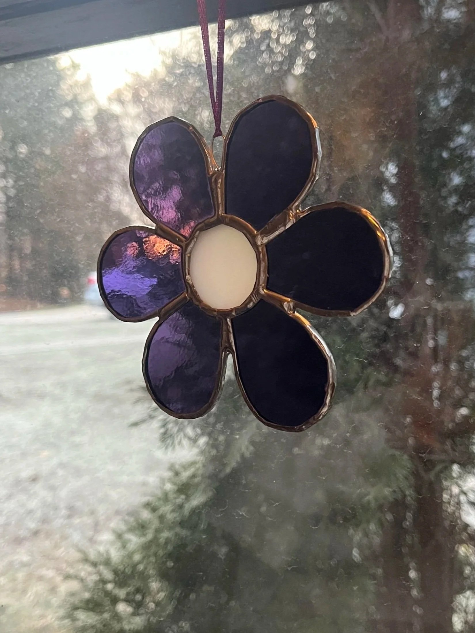 A stained glass flower with purple petals and a white center hanging in a window