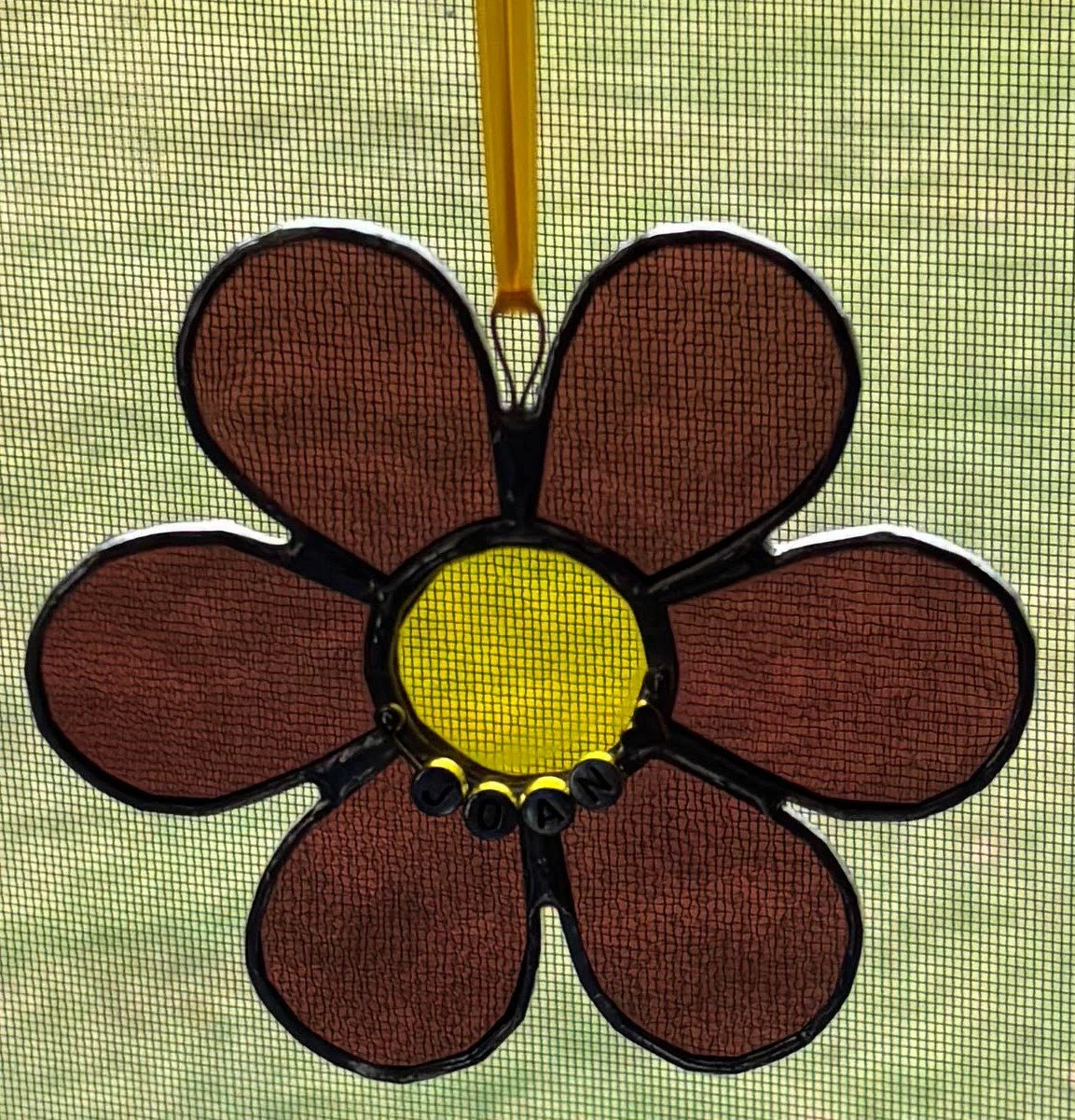 A children's trampoline with a flower-shaped safety enclosure featuring six brown petals, a yellow center, and black edges, with a yellow pole supporting the structure.