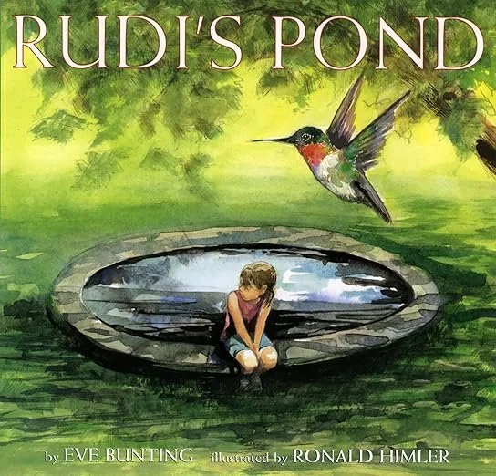 Book cover titled 'RUDI'S POND' featuring a young girl sitting by a pond with a stone border, and a colorful hummingbird flying above it, surrounded by green leaves.