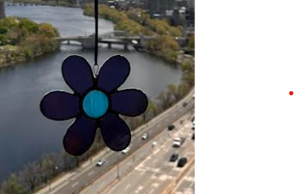 A blue stained glass flower hangs on a window overlooking a river