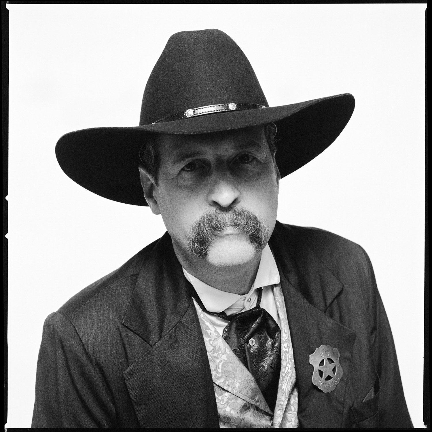 Black and white portrait of a man dressed as a sheriff, wearing a large cowboy hat, a sheriff's badge, and Western-style clothing. Pella, Iowa Tulip Time Festival, Dutch Heritage, Wyatt Earp