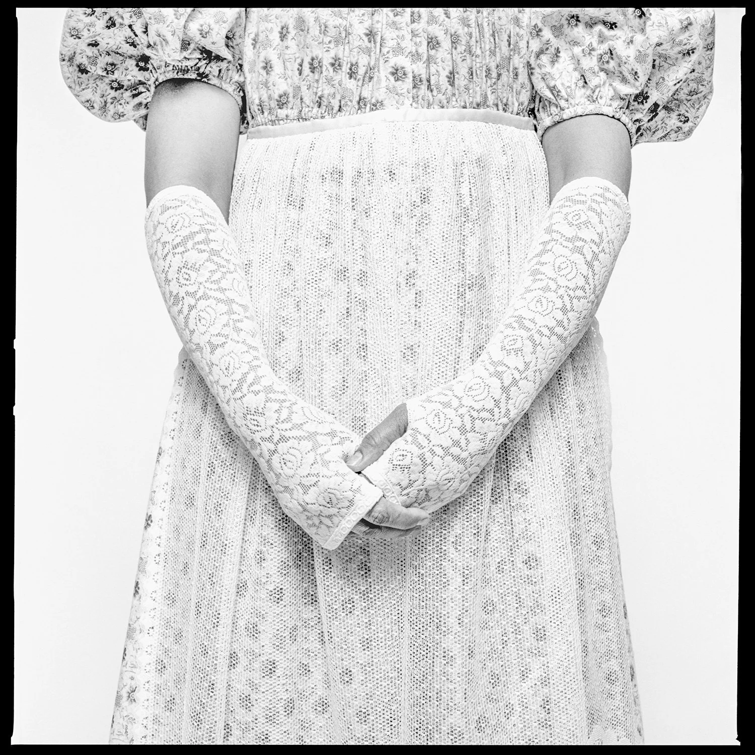 A person dressed in vintage clothing, wearing long lace gloves and a floral dress, standing against a plain background. Pella, Iowa Tulip Time Festival, Dutch Heritage