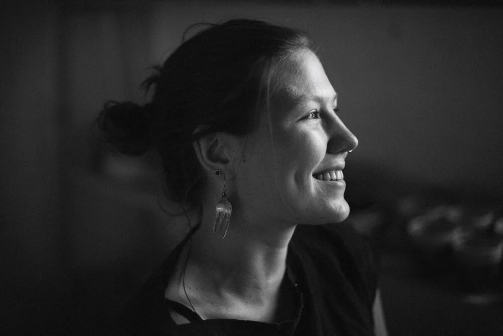 Profile of a smiling woman pottery artist with swept-back hair and a dark top, looking to the right, in black and white.