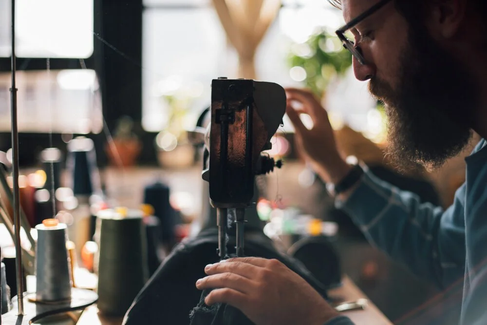 Textile artist working with a sewing machine in a workshop, surrounded by spools of thread.