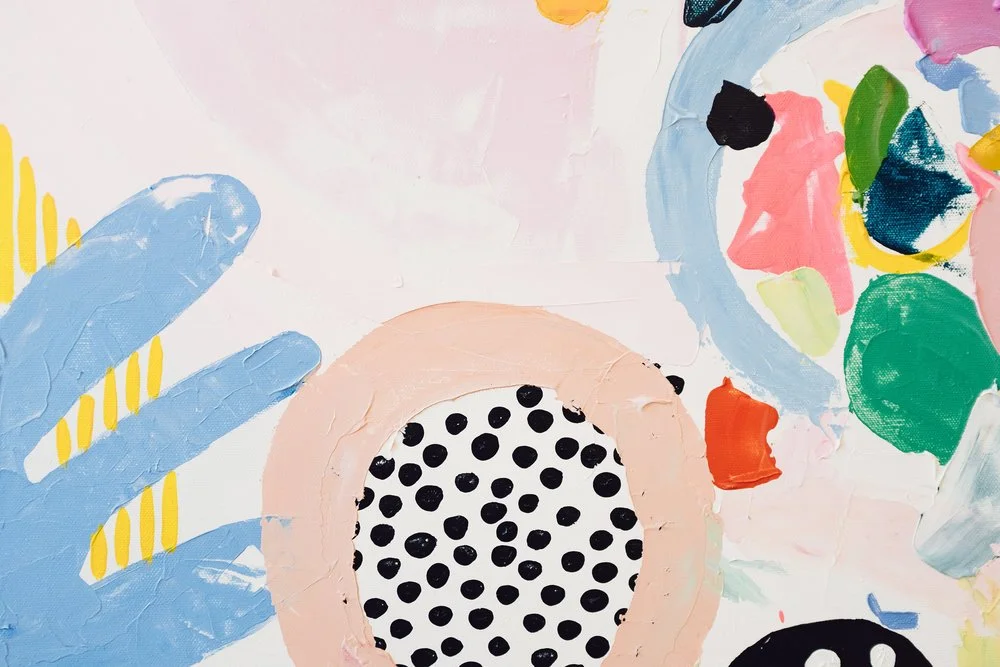 Close-up of an abstract, colorful painting with a blue hand, a polka-dotted circle, and various vibrant blotches of paint.