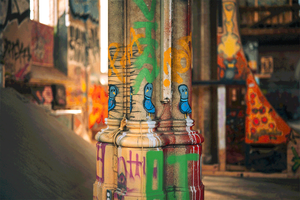 graffiti-covered wooden pillar with cartoonish blue characters in an urban setting Sk8 Liborius