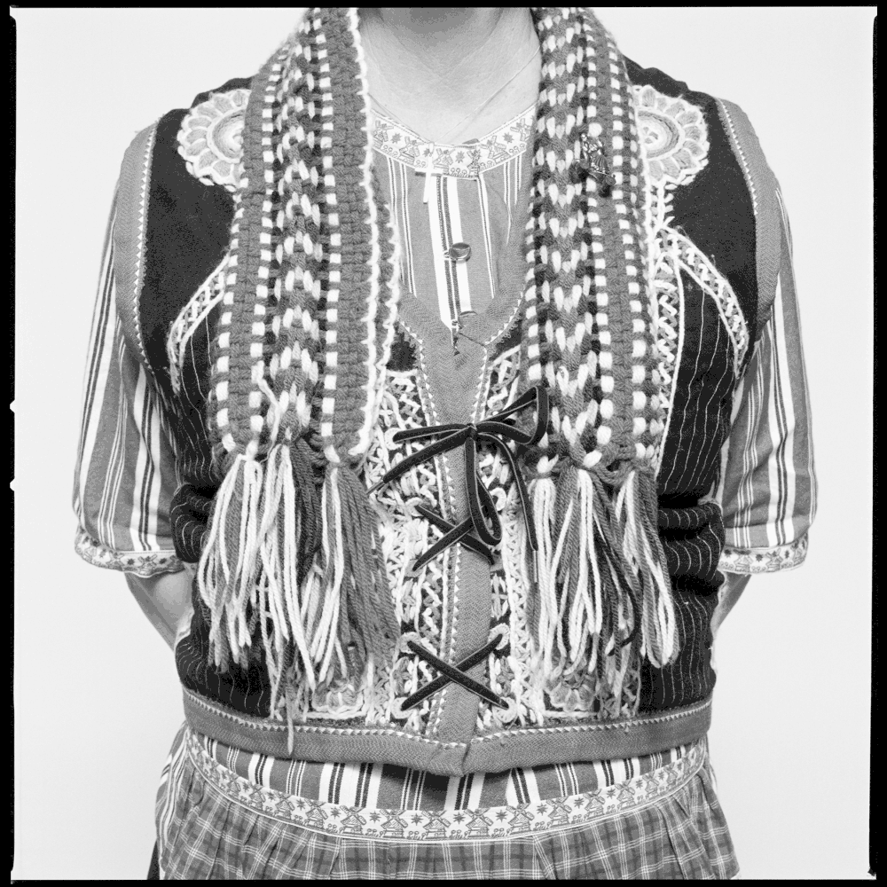 The image shows a person wearing a traditional or folk-style outfit with detailed embroidery, patterned clothing, and braided hair. Pella, Iowa Tulip Time Festival, Dutch Heritage