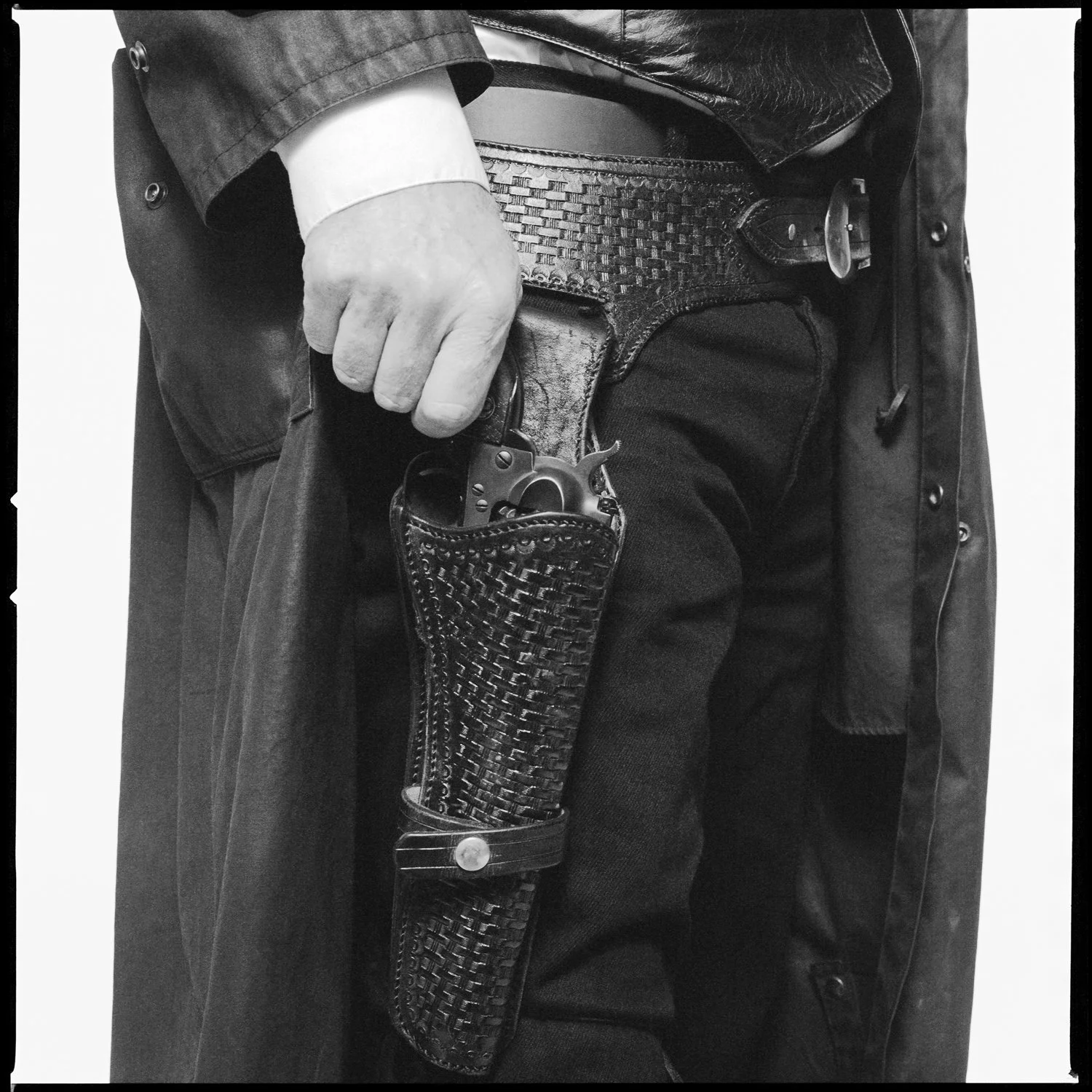 A person wearing a dark jacket and jeans with a leather belt, holding a revolver in a woven leather holster attached to their belt. Pella, Iowa Tulip Time Festival, Dutch Heritage, Wyatt Earp