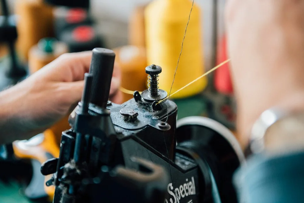 Textile artist man sewing or repairing using a sewing machine with yellow thread.
