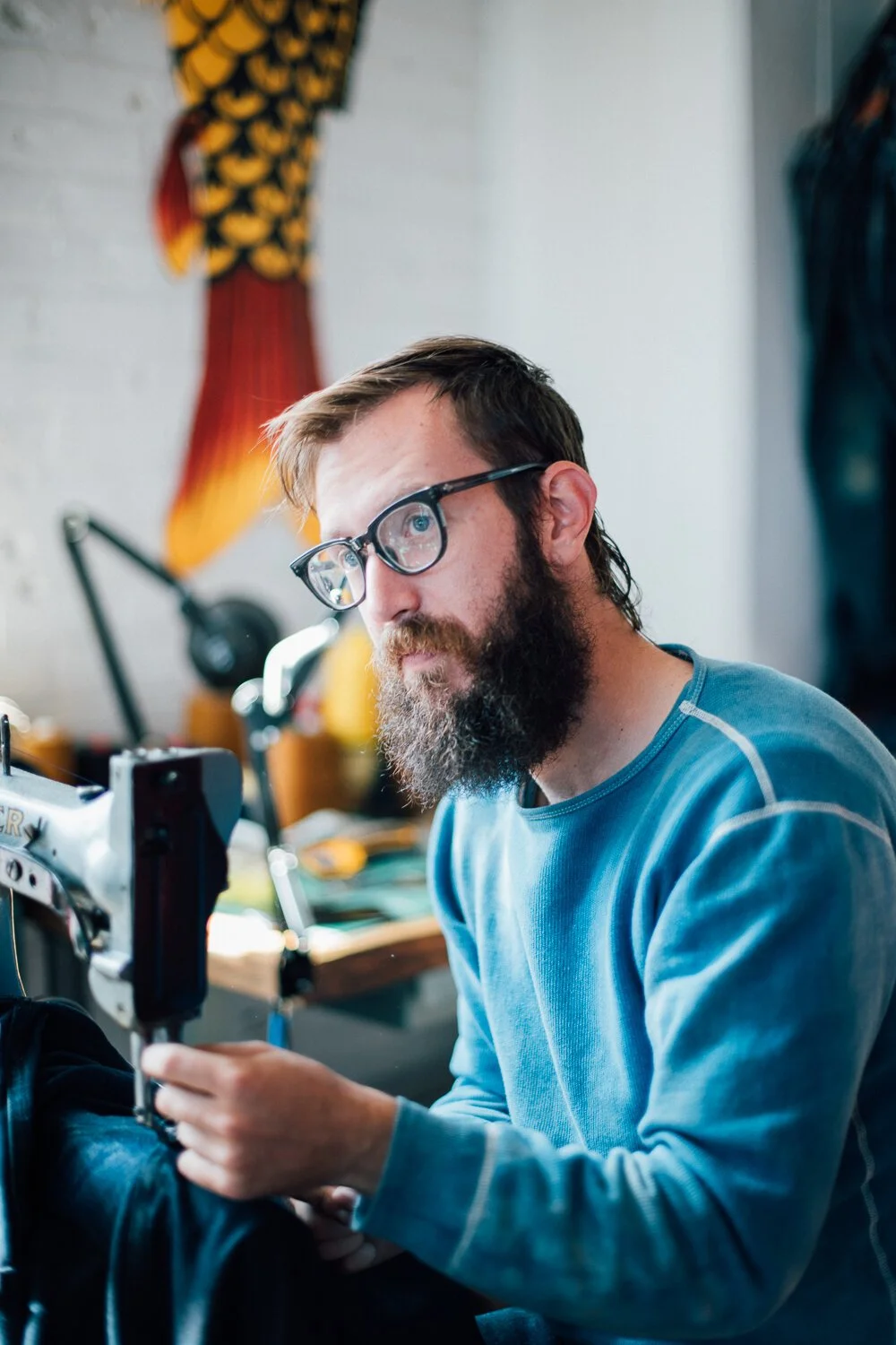 Textile artist man with glasses and a beard working on a sewing machine in a workshop.