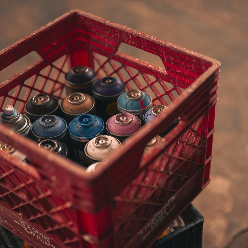 Red shopping basket filled with spray paint cans in various colors. Sk8 Liborius