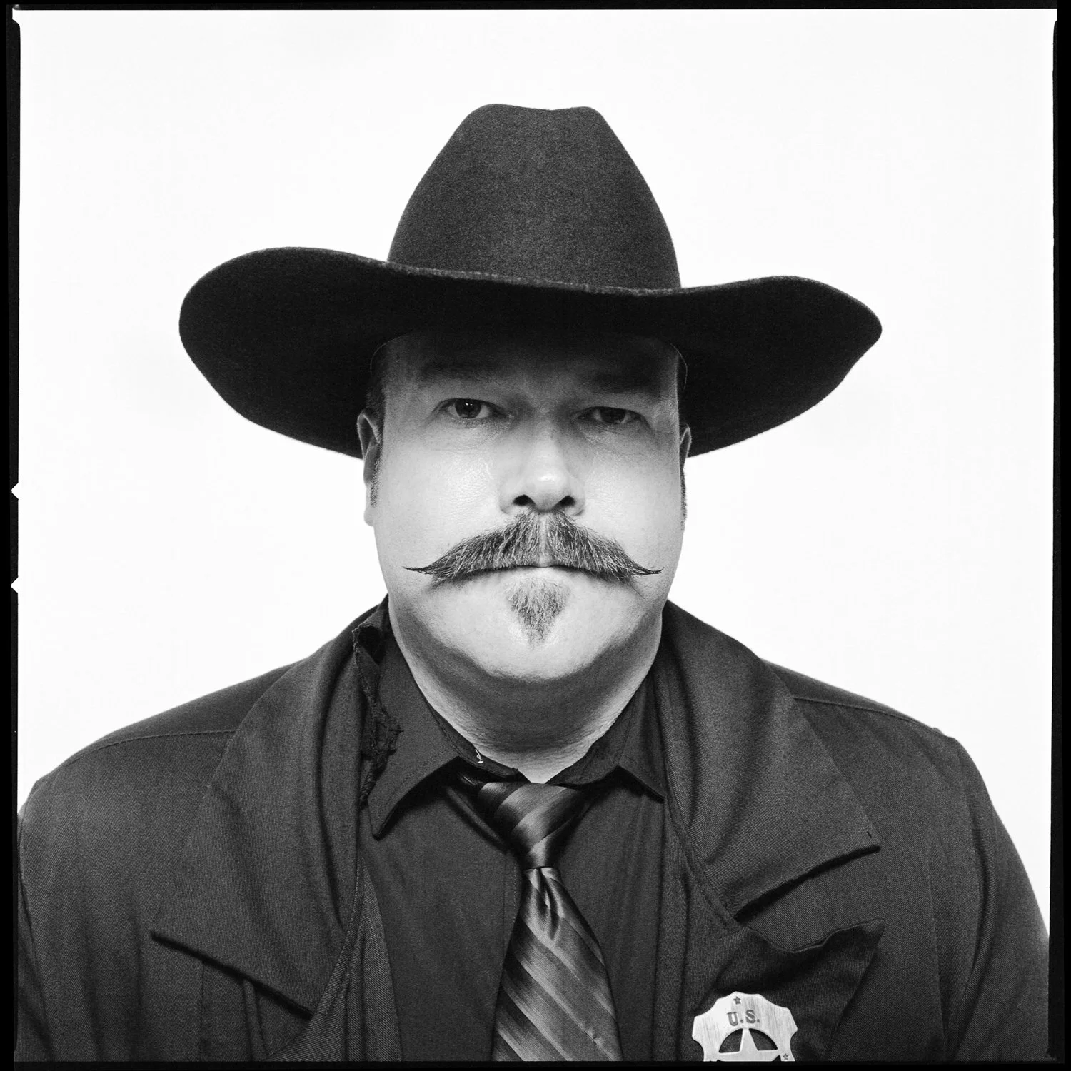 A man with a thick mustache and small goatee wearing a cowboy hat, dark shirt, tie, and sheriff badge. Pella, Iowa Tulip Time Festival, Dutch Heritage, Wyatt Earp