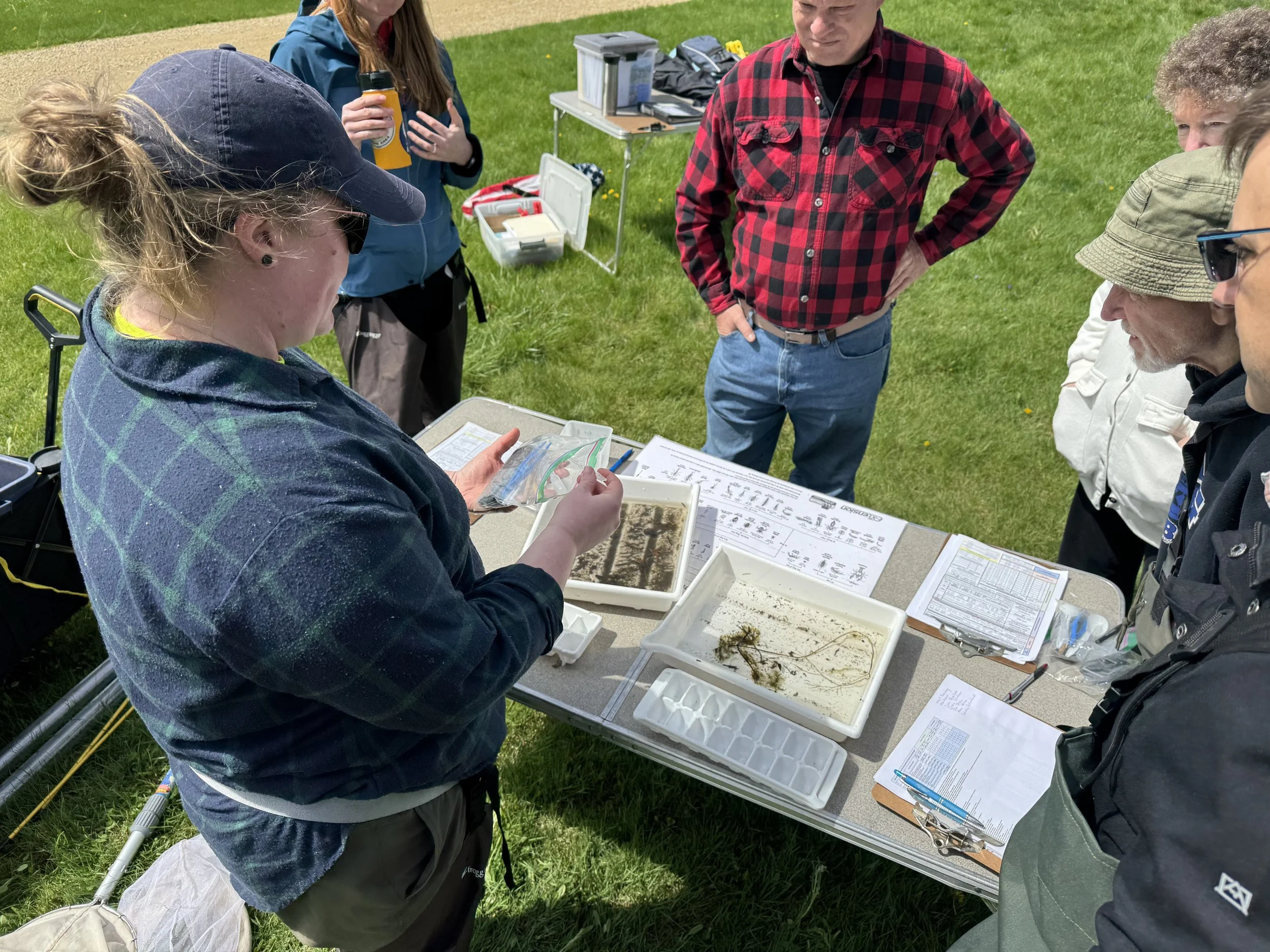 Instruction on assessing Biotic Index and presence of Aquatic Invasive Species (AIS); shown instructors explaining the process of identifying and classifying and scoring organisms using visual keys of species representative of 'good', 'fair', and 'po