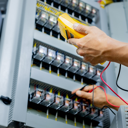 Person using a yellow multimeter to test a control panel with multiple relays.
