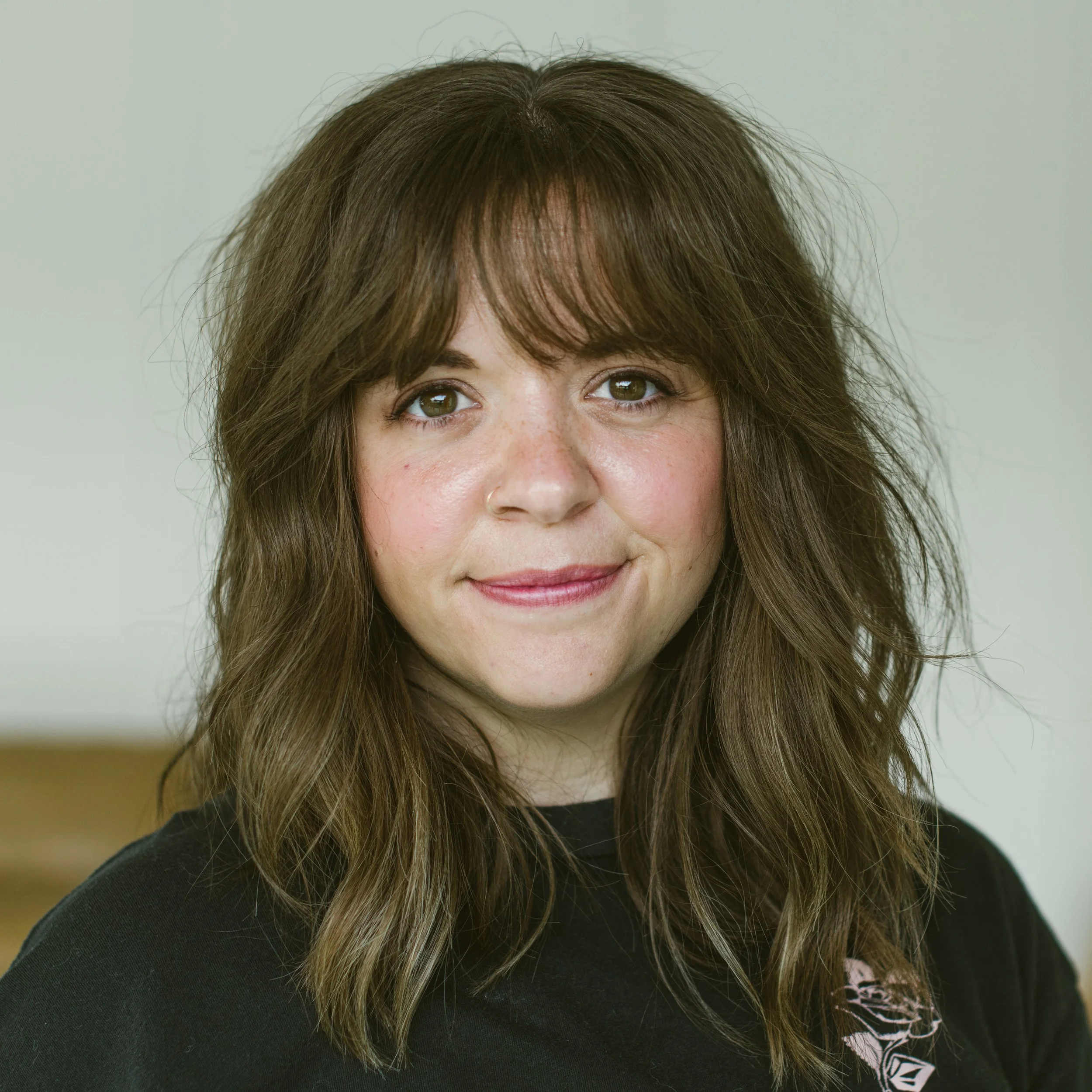 Smiling woman with tattoo, wearing white tank top, outdoors with city skyline in background.