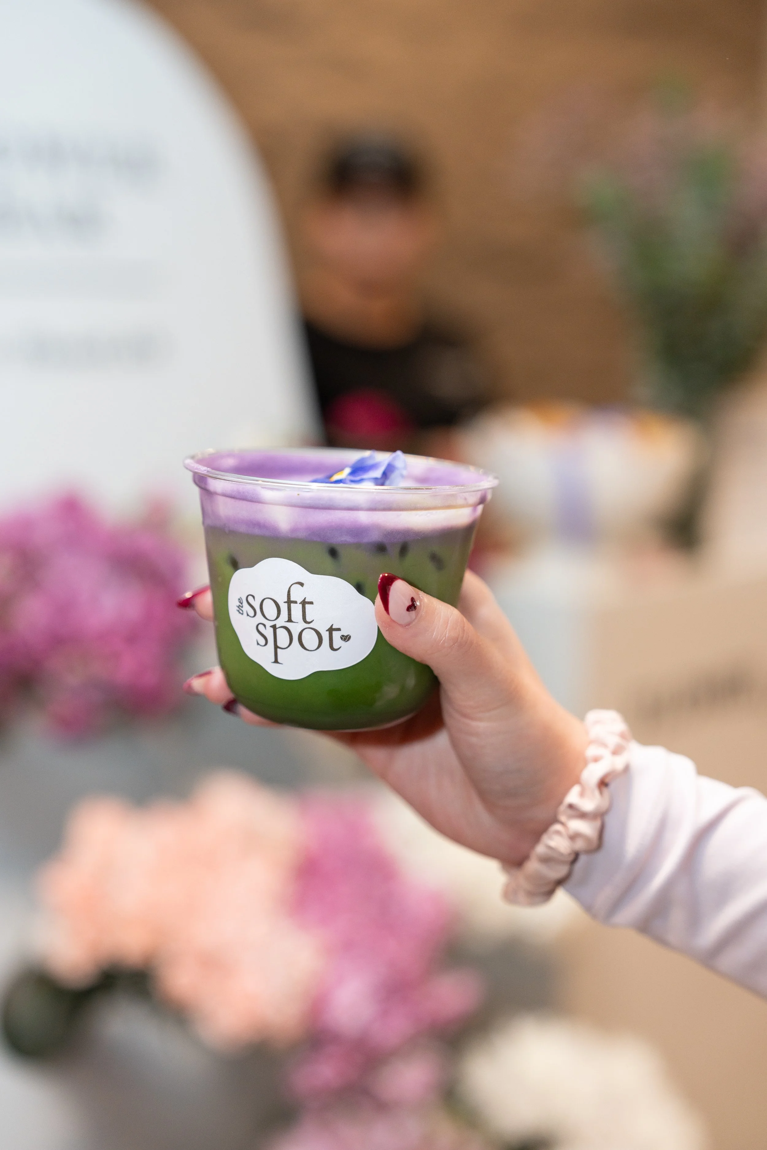 Guest's hand holding an iced matcha drink topped with an edible flower, prepared by The Soft Spot for a catered event