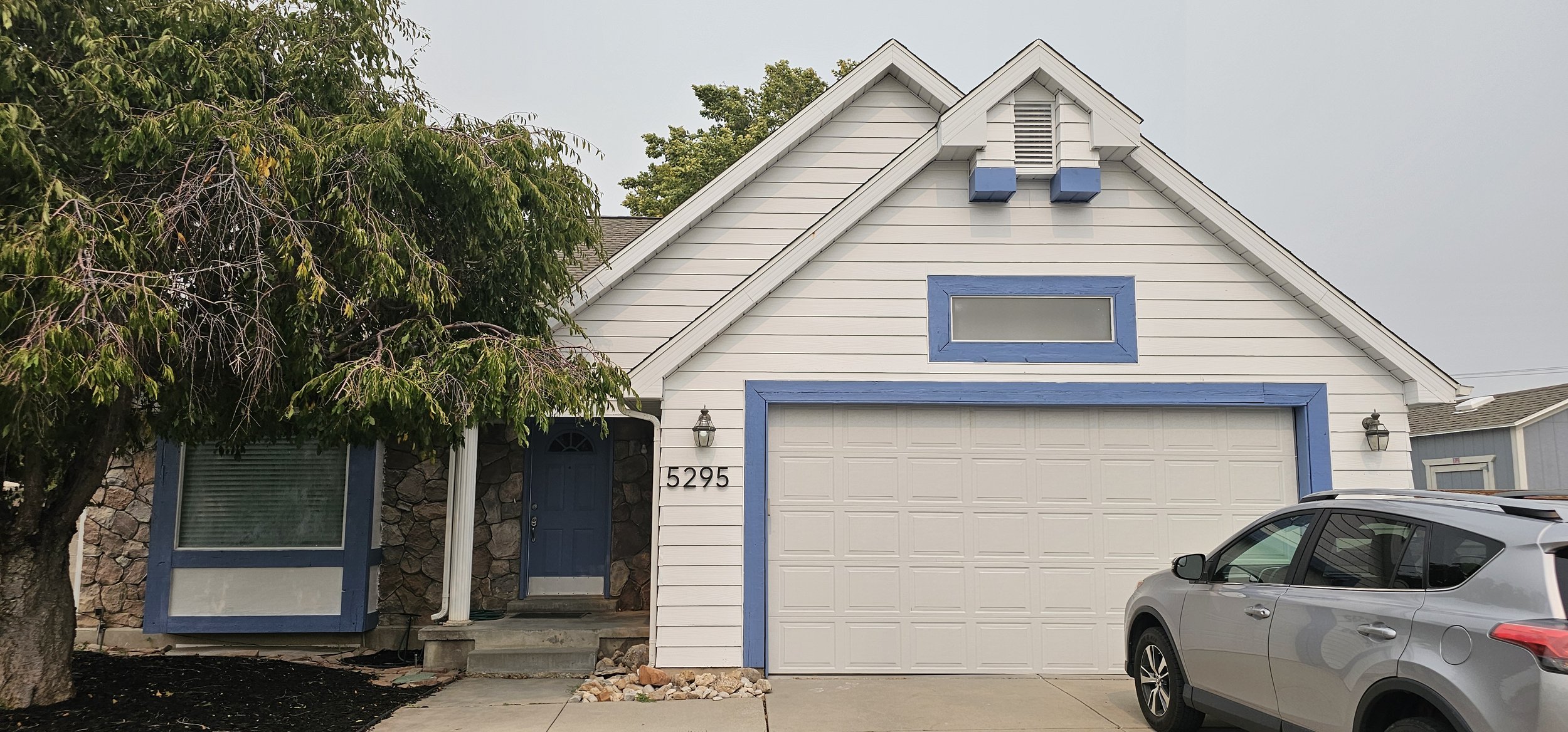 The front of a house freshly painted white with light blue trim, a car in the driveway.