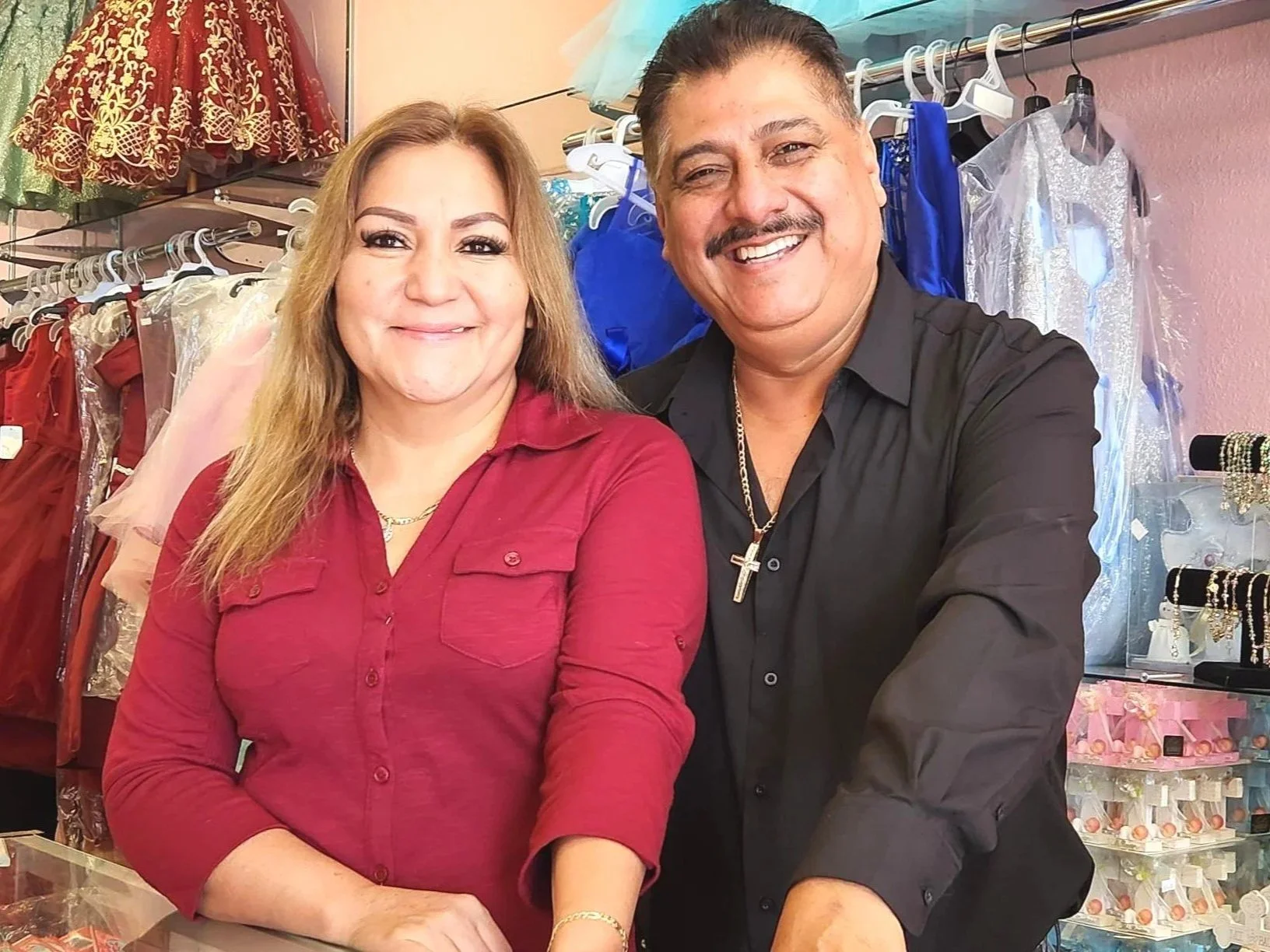 Smiling man and woman standing inside a clothing store with dresses and jewelry displayed behind them. Westwood, Denver, CO Business owners