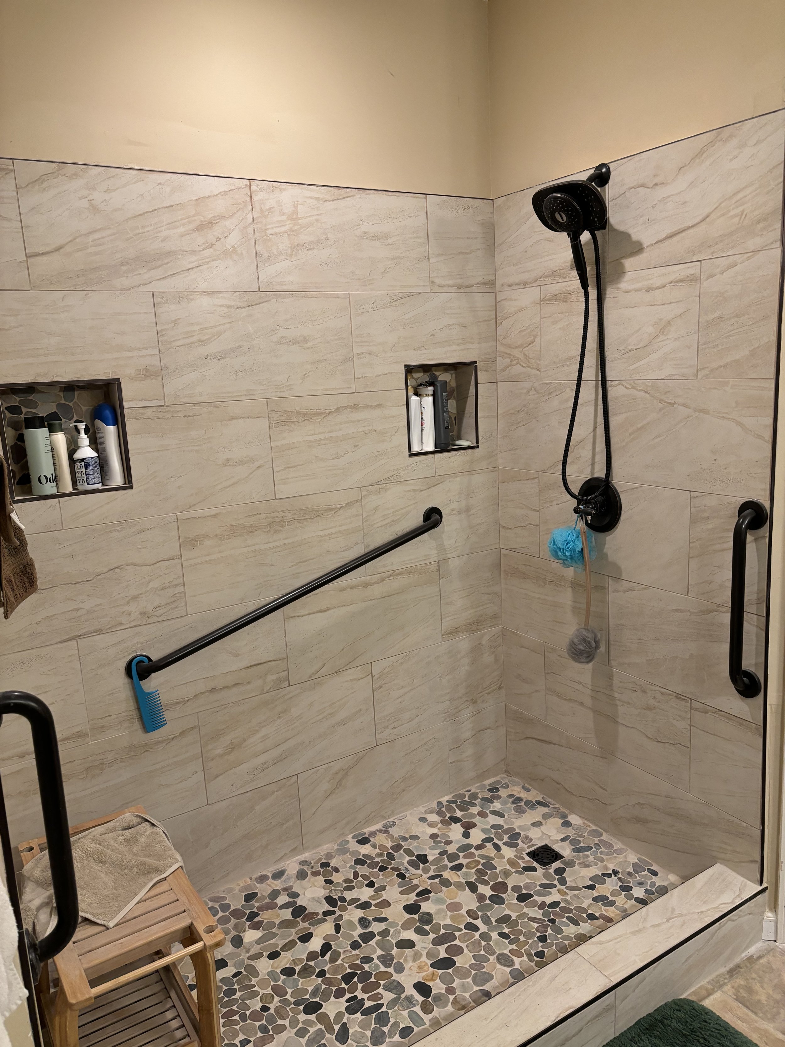 Zero-entry shower with sleek black finishes on grab bars, showerhead, and fixtures.