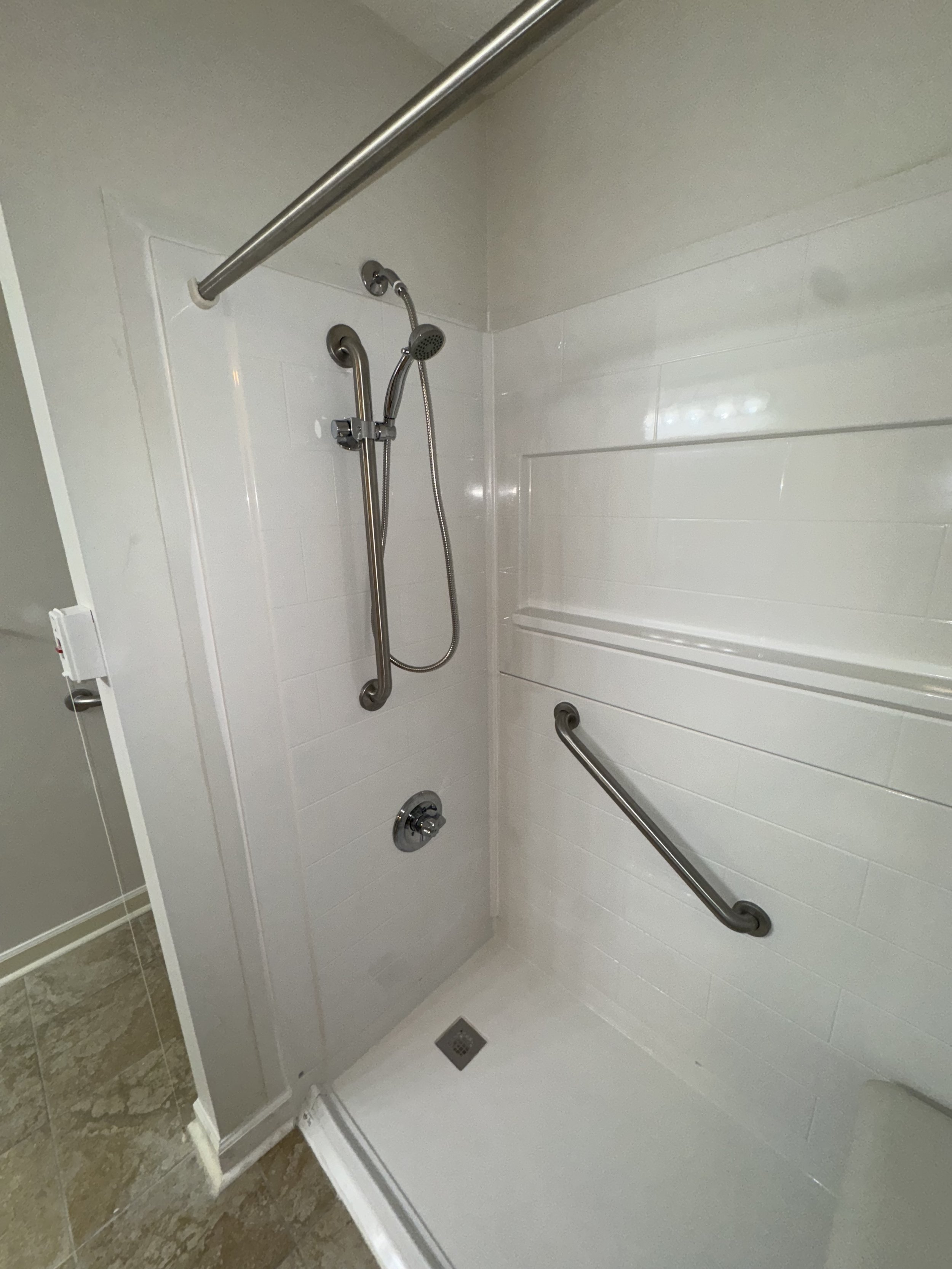 Close-up of zero-entry shower highlighting showerhead, non-slip tiles, and grab bar for safety and accessibility.