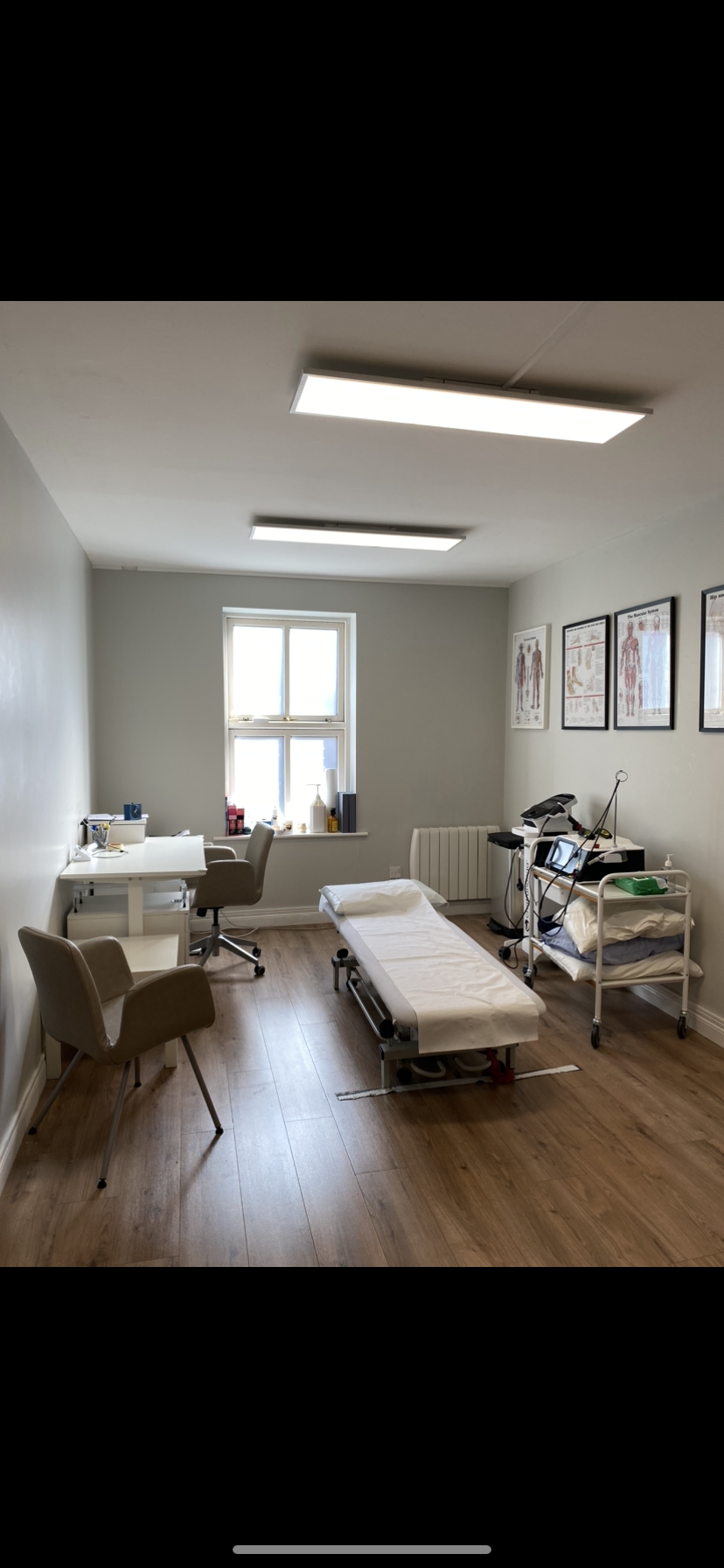 Medical examination room with an examination table, chairs, medical equipment, and charts on the wall.